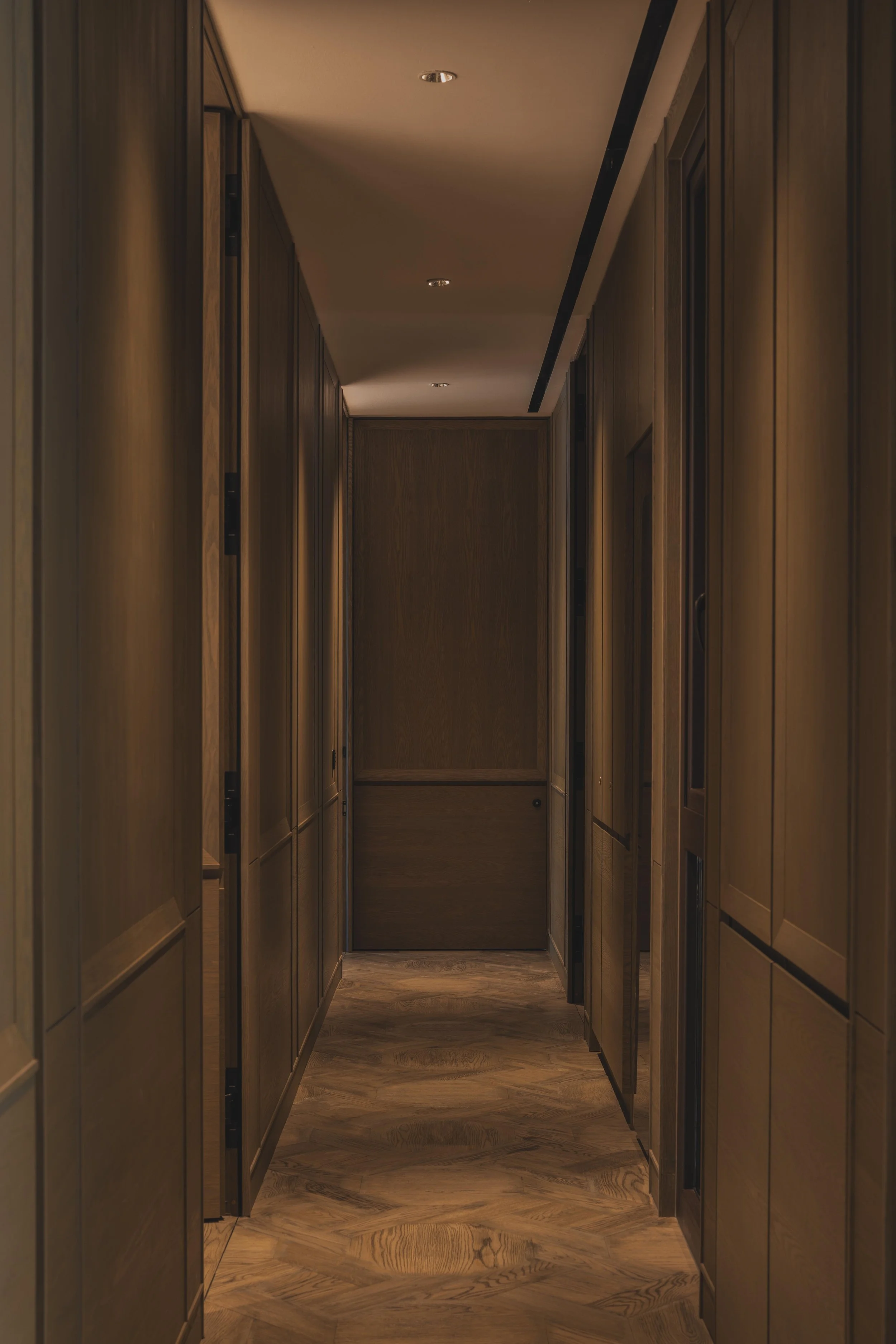 Wooden hallway with cabinets and a wooden floor, softly lit ceiling lights, and a door at the end.