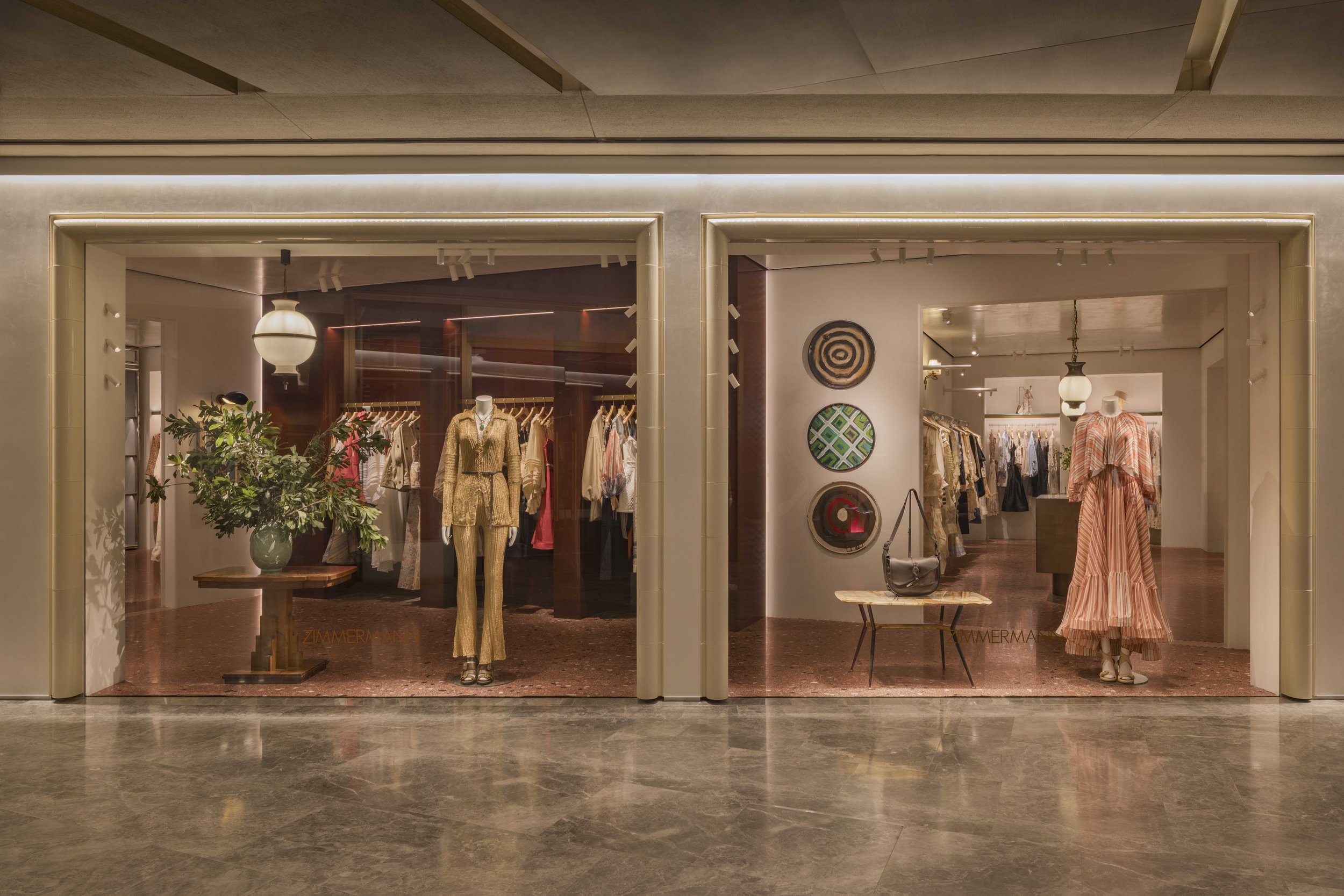 Clothing store window display with mannequins dressed in stylish outfits, and decorative artwork on the wall inside.