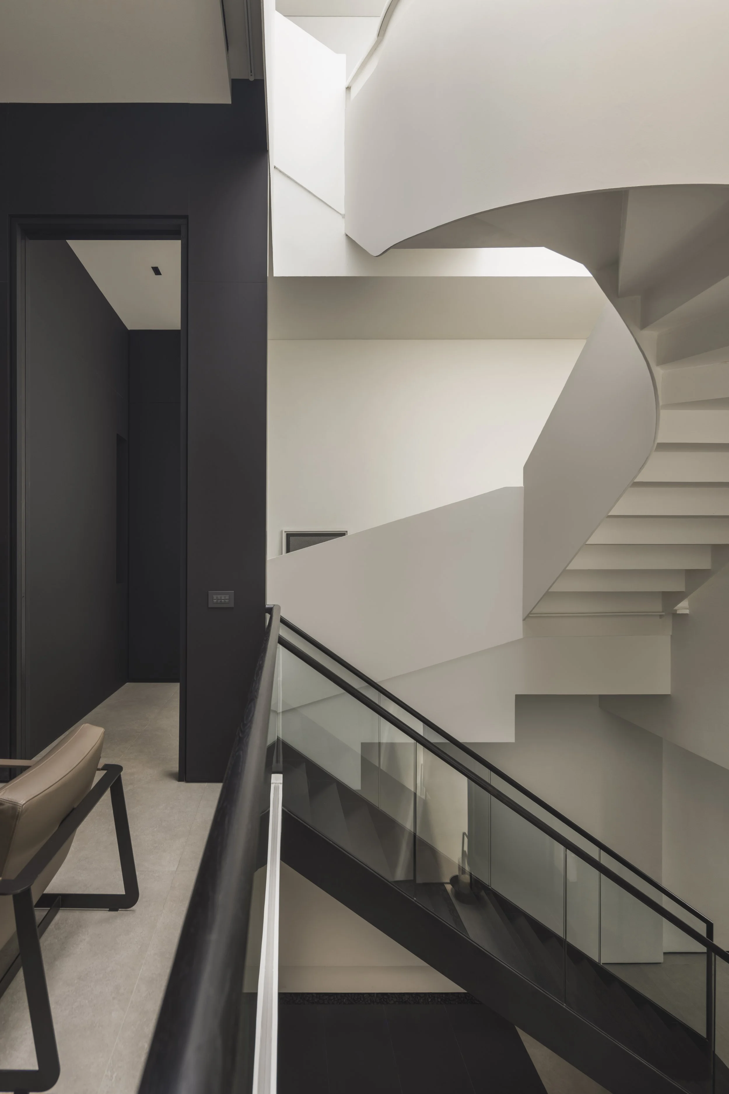 Modern interior staircase with white walls, black accents, and a glass railing, viewed from below.