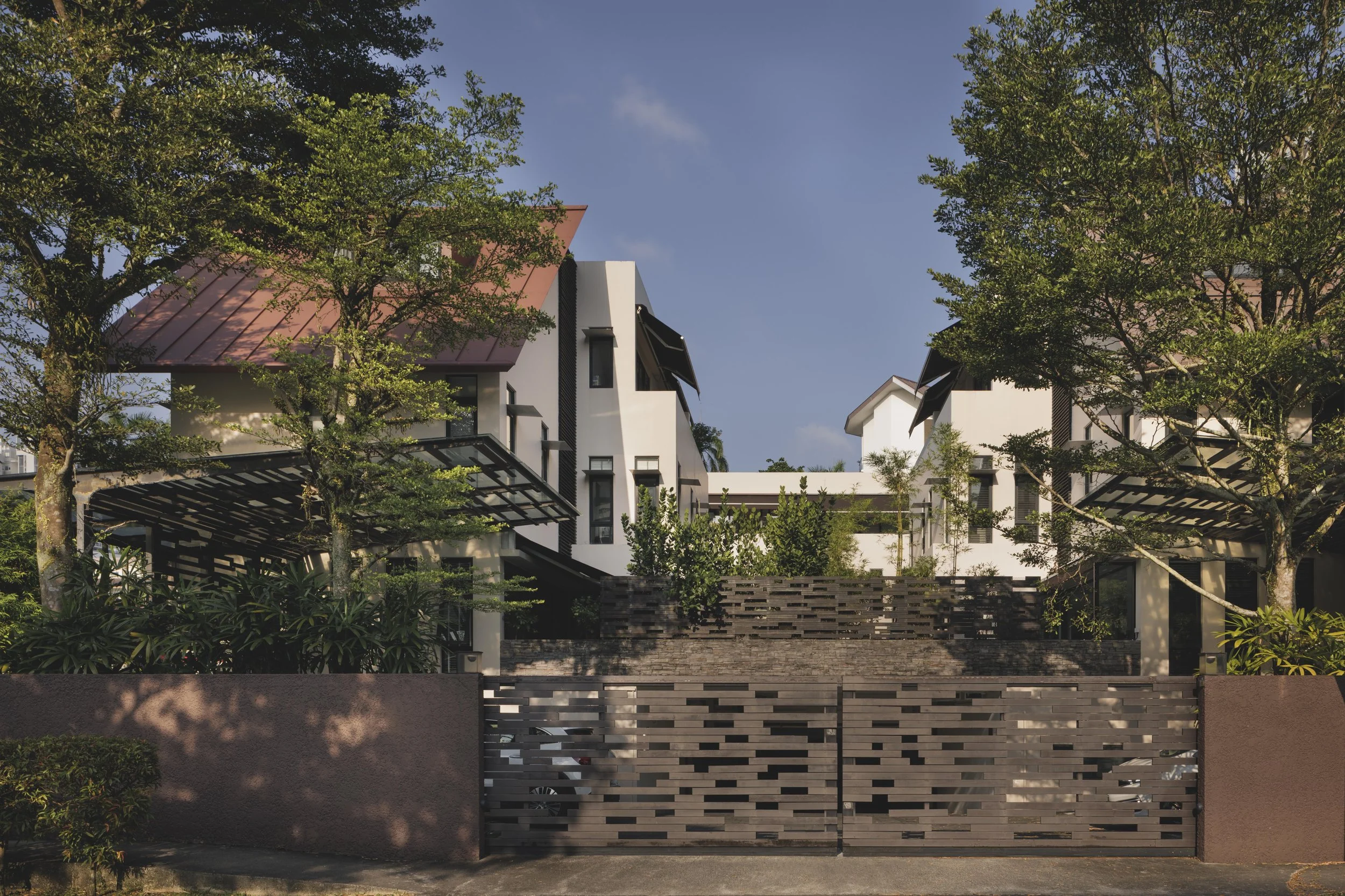 Modern white residential buildings with red and black roofs, surrounded by green trees and foliage, under a clear blue sky.