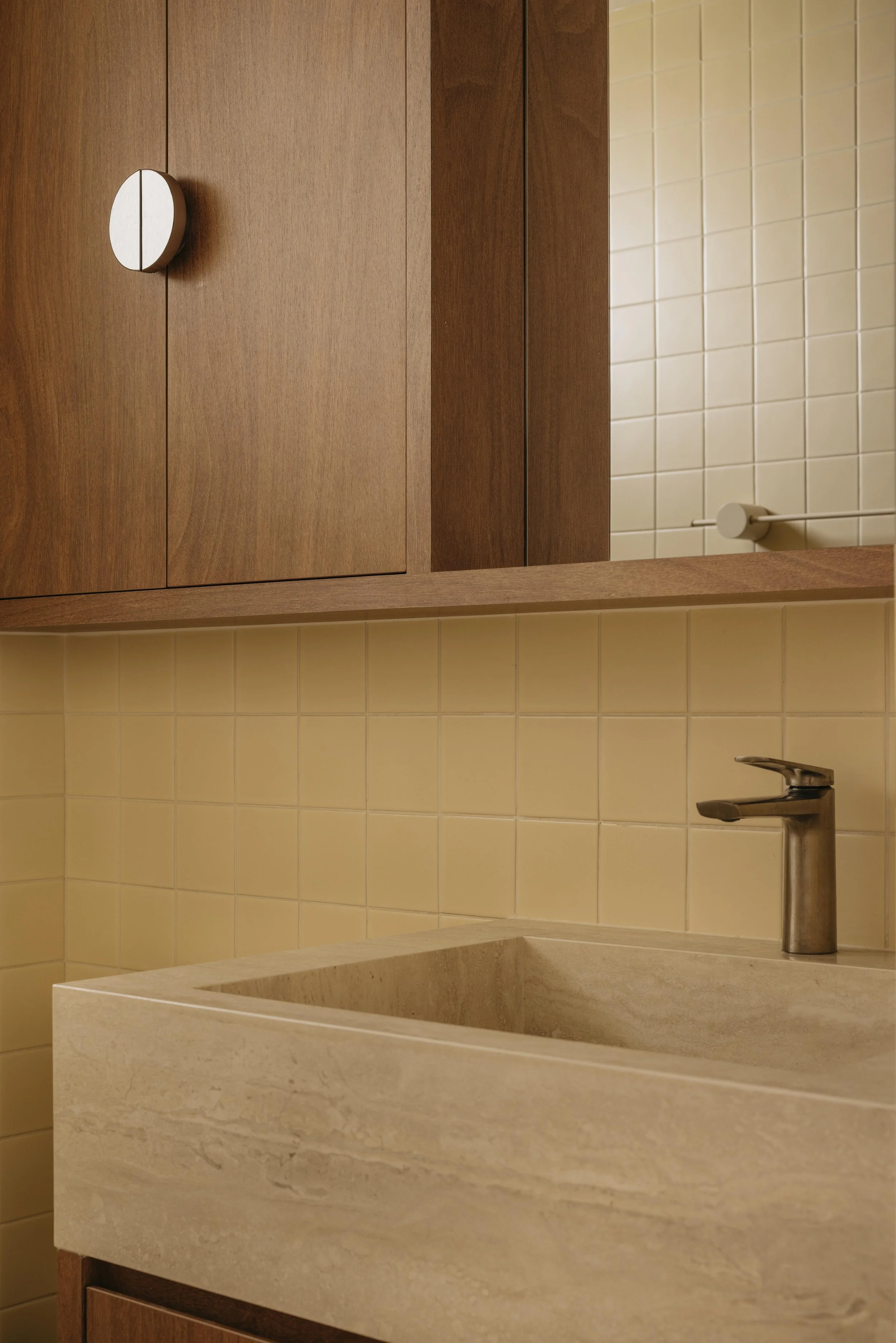 A bathroom vanity with a stone sink, a silver faucet, wooden cabinets, and a wall with beige tiles.