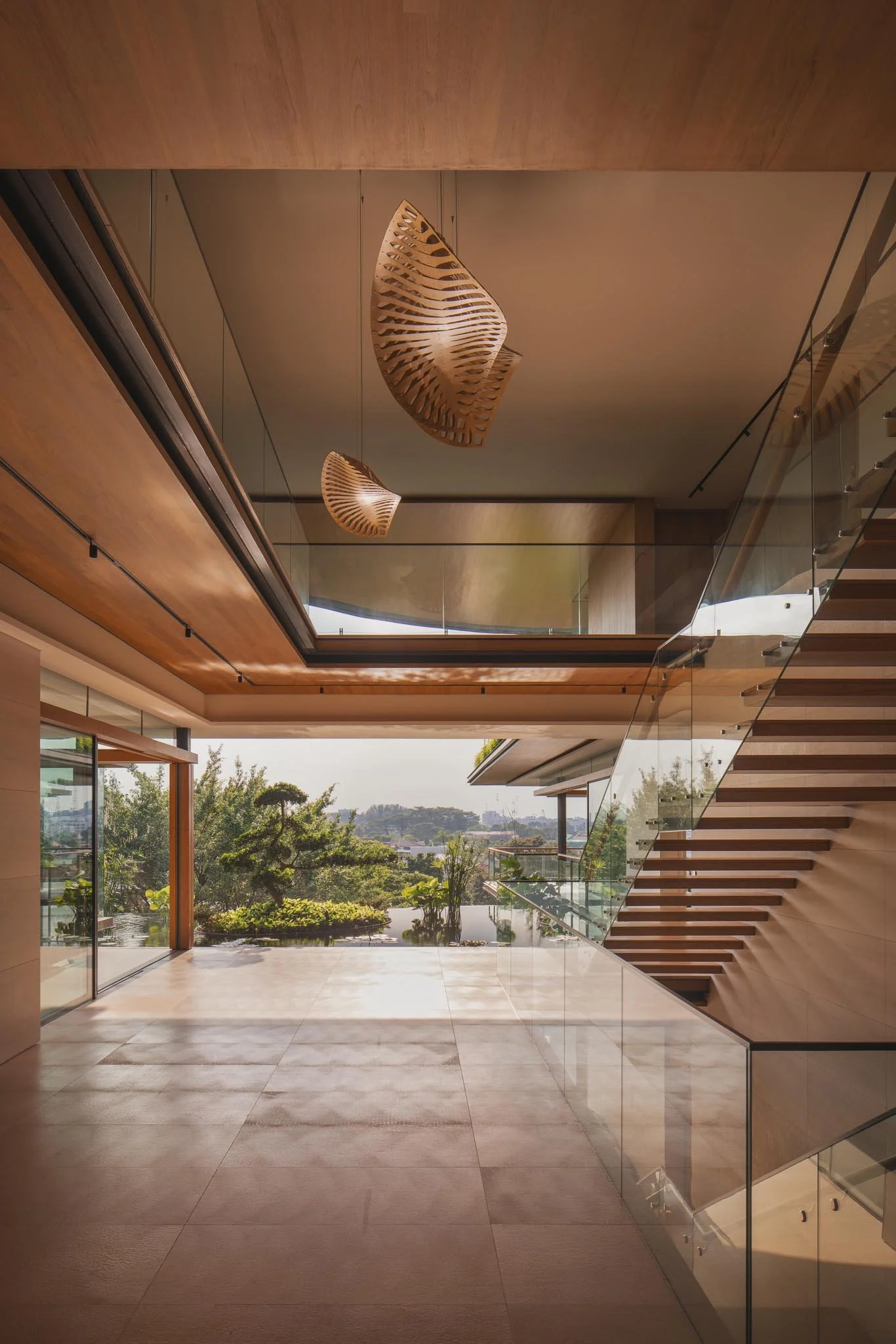 Modern interior with a staircase on the right, large glass windows on the left showing a view of trees and a distant cityscape. Wooden ceiling and walls, hanging wooden light fixtures.