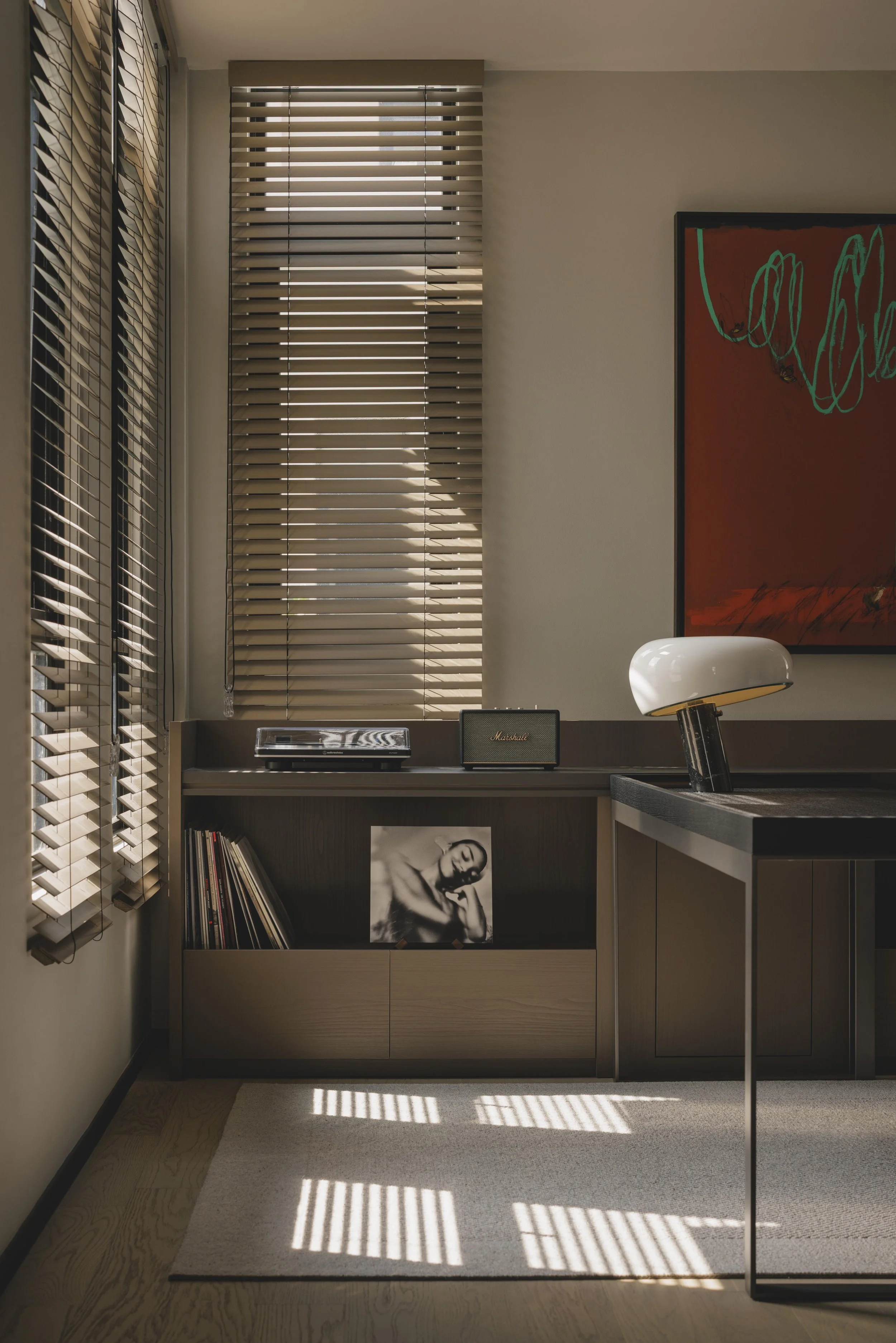 Interior of a modern room with window blinds, a sideboard holding a record player and a Marshall speaker, and a black-and-white portrait photo of a woman.