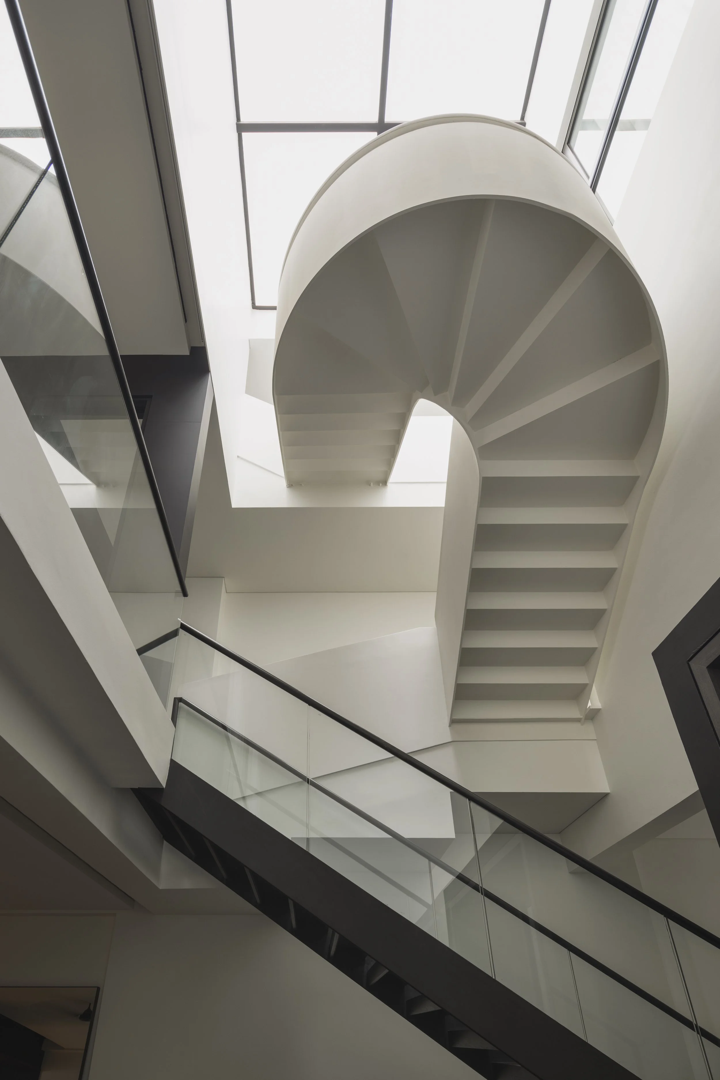 Interior view of a modern building with a white spiral staircase, large windows, and glass railings.