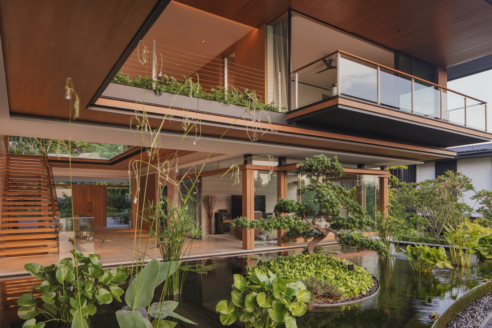 Modern house with large glass windows and balconies, surrounded by lush plants and water features with lily pads in the foreground.