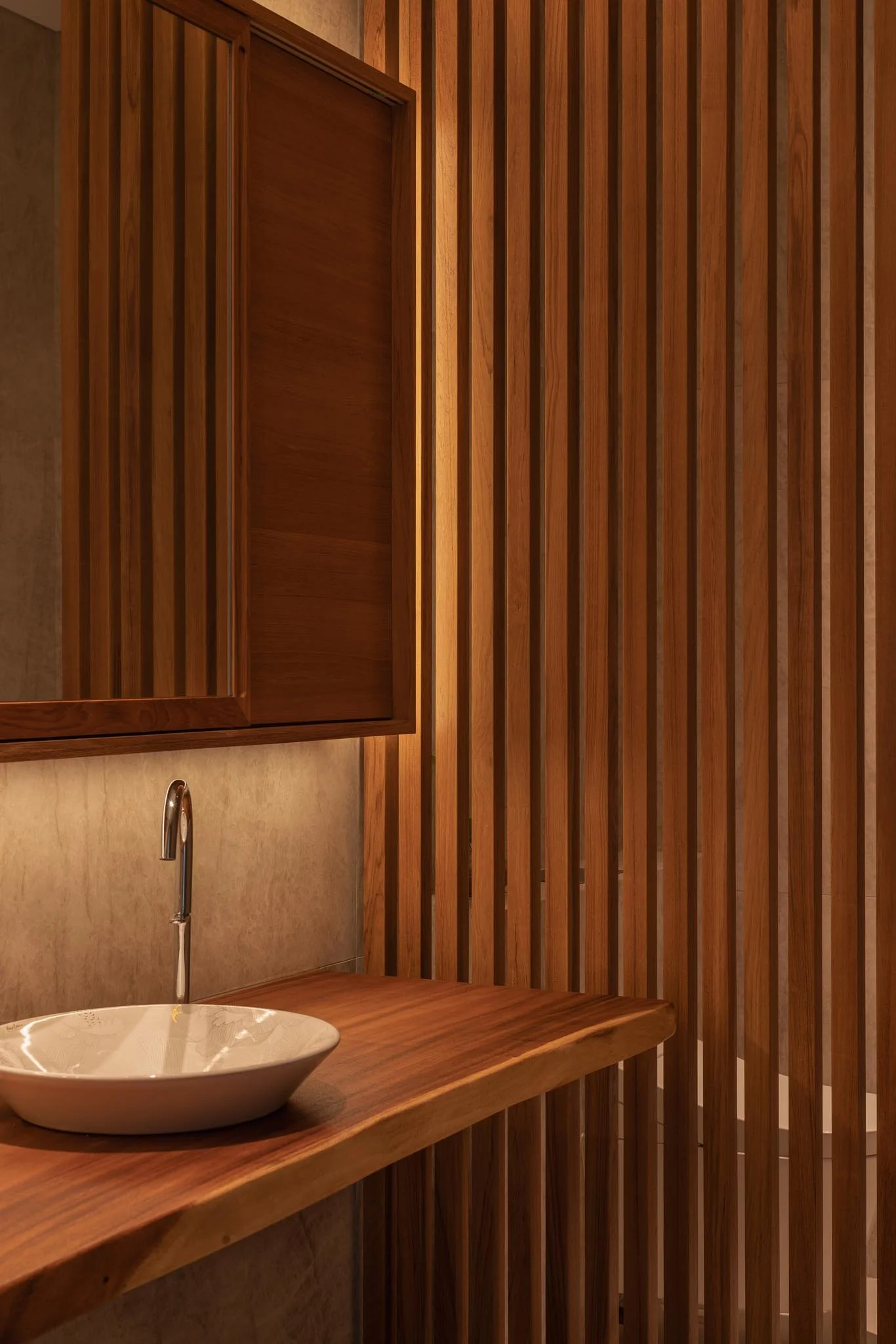 Interior of a room with wooden walls, a small sink with a chrome faucet, a wooden countertop, and a mirror with a wooden frame.