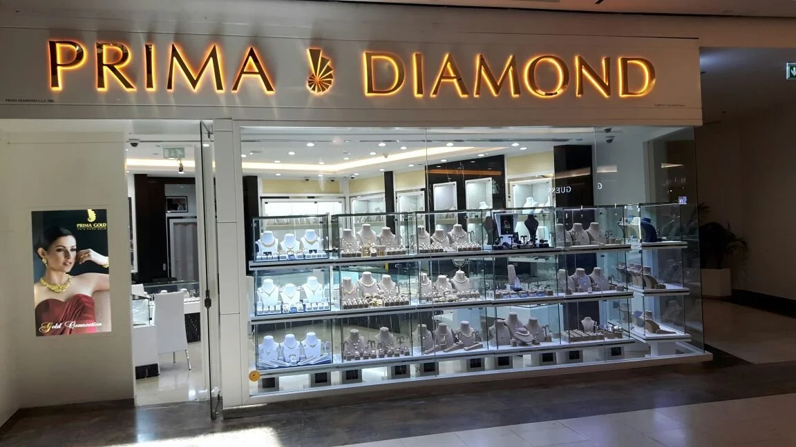 Jewelry store named Prima Diamond with glass display cases filled with necklaces, earrings, and rings, and a promotional poster featuring a woman wearing jewelry.