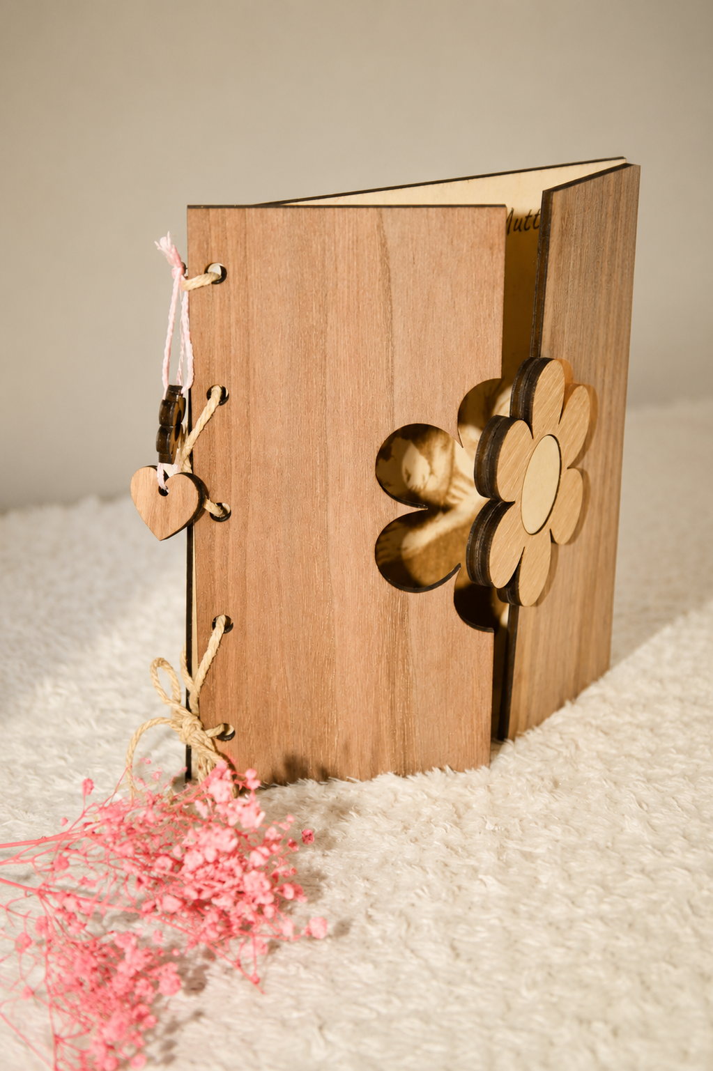 Ein Holzbuch mit einer Blume in Scherenschnitt und einer rosa Trockenblume davor.