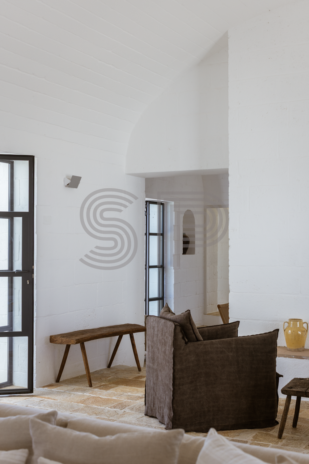 Light-filled contemporary interior with high vaulted ceiling, textured white walls and stone flooring.