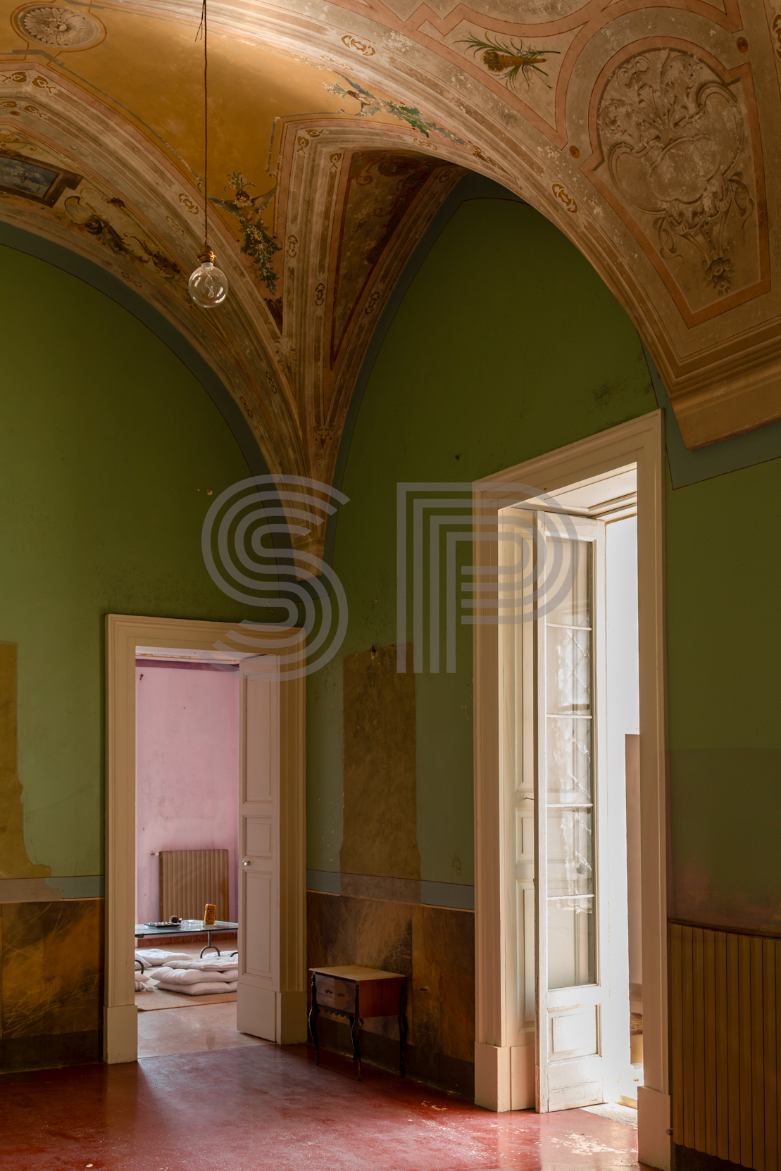 Green palazzo room with ornate frescoed vaulted ceiling, tall French doors and faded decorative finishes.