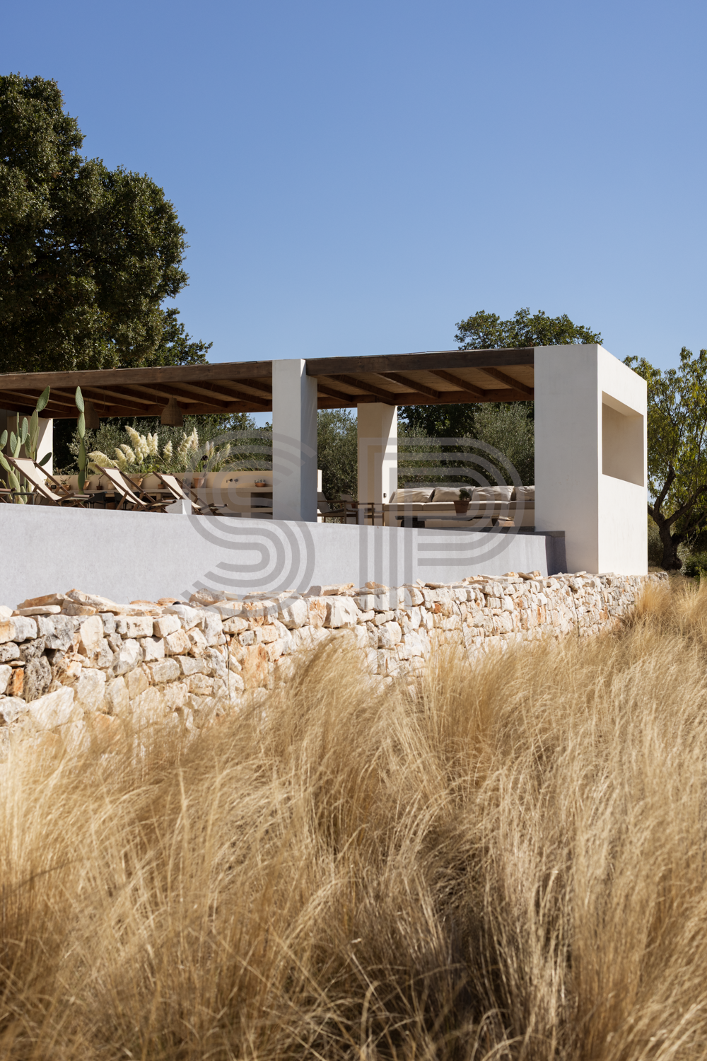 Contemporary white villa in Puglia with minimalist geometric architecture, traditional dry-stone wall and natural Mediterranean planting