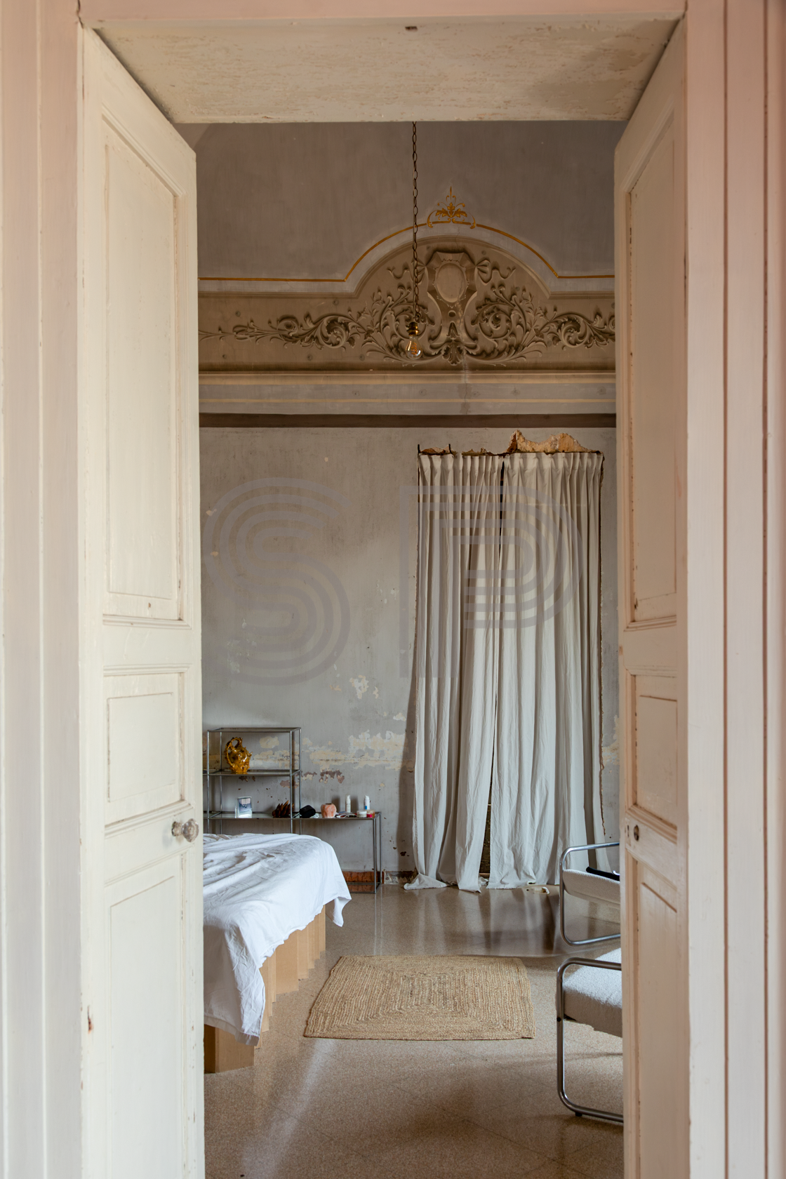 Palazzo bedroom viewed through tall double doors with decorative plasterwork and distressed walls.