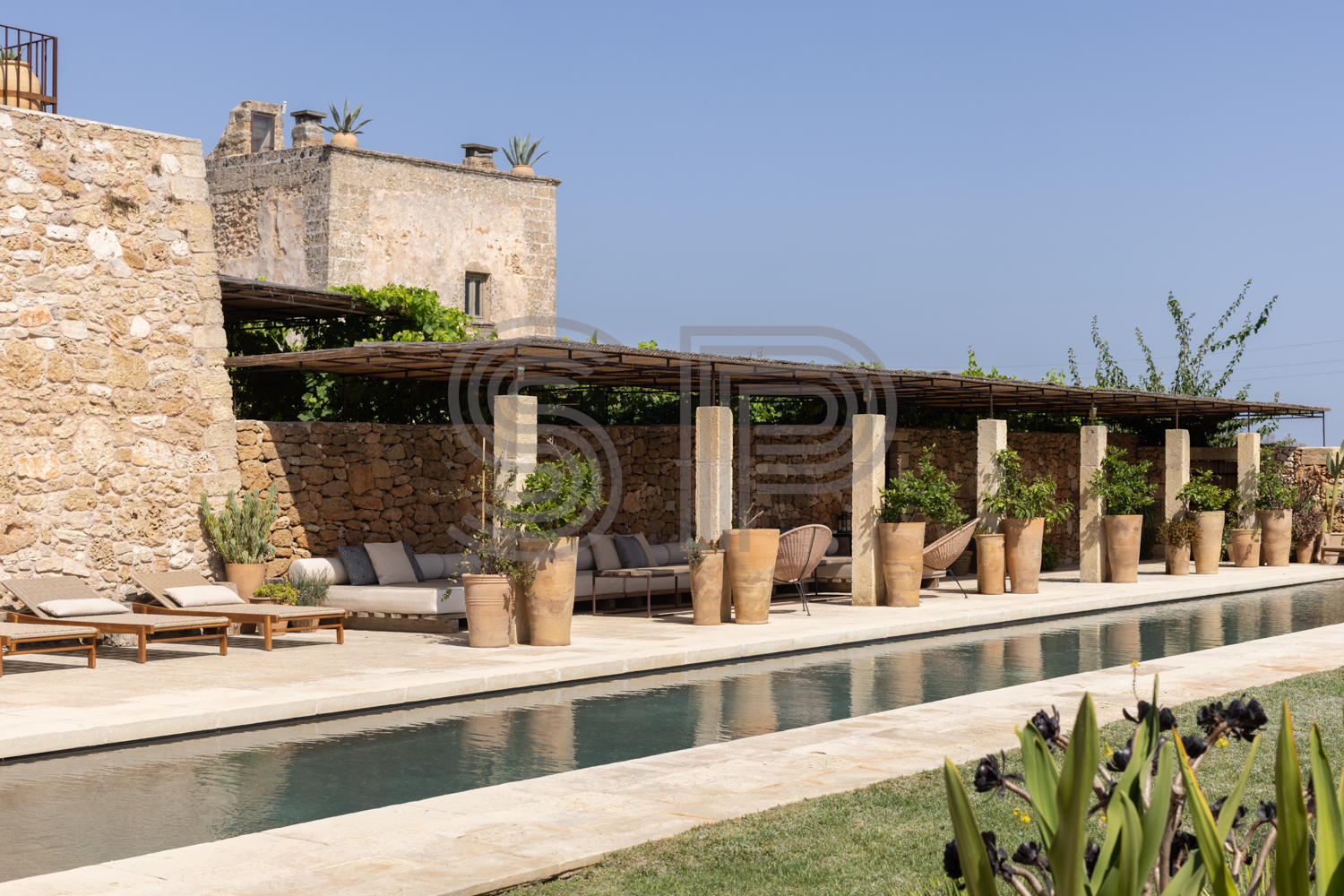Large swimming pool beside traditional Puglian stone architecture with covered outdoor seating.