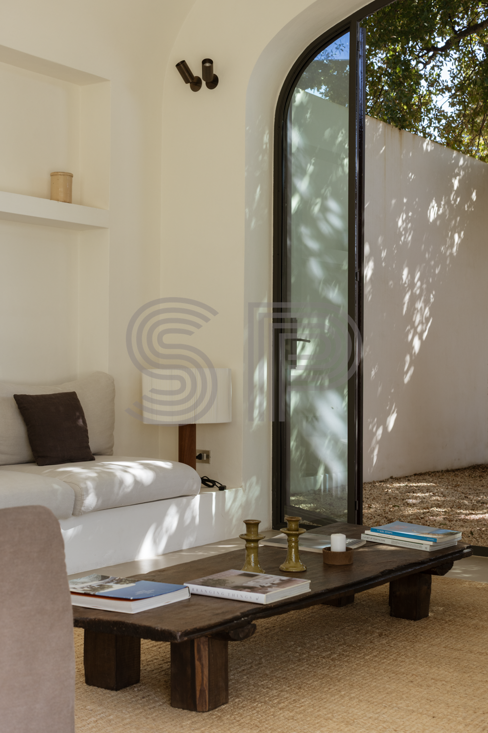 Minimalist Puglia villa interior with white plaster walls, large arched glass doorway, built-in seating and soft natural light