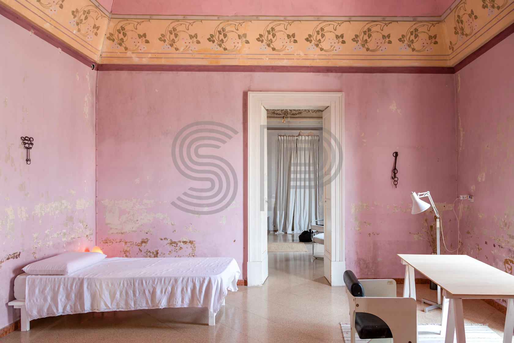 Pink palazzo bedroom with distressed plaster walls, decorative painted frieze and high ceilings.
