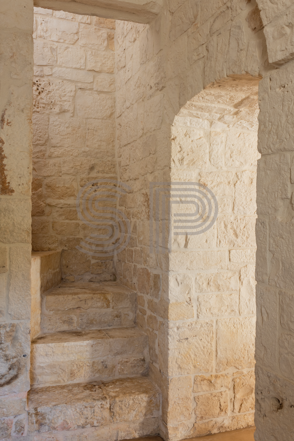 Traditional Trullo interior in Puglia with exposed local stone walls, built-in stone staircase and warm natural textures