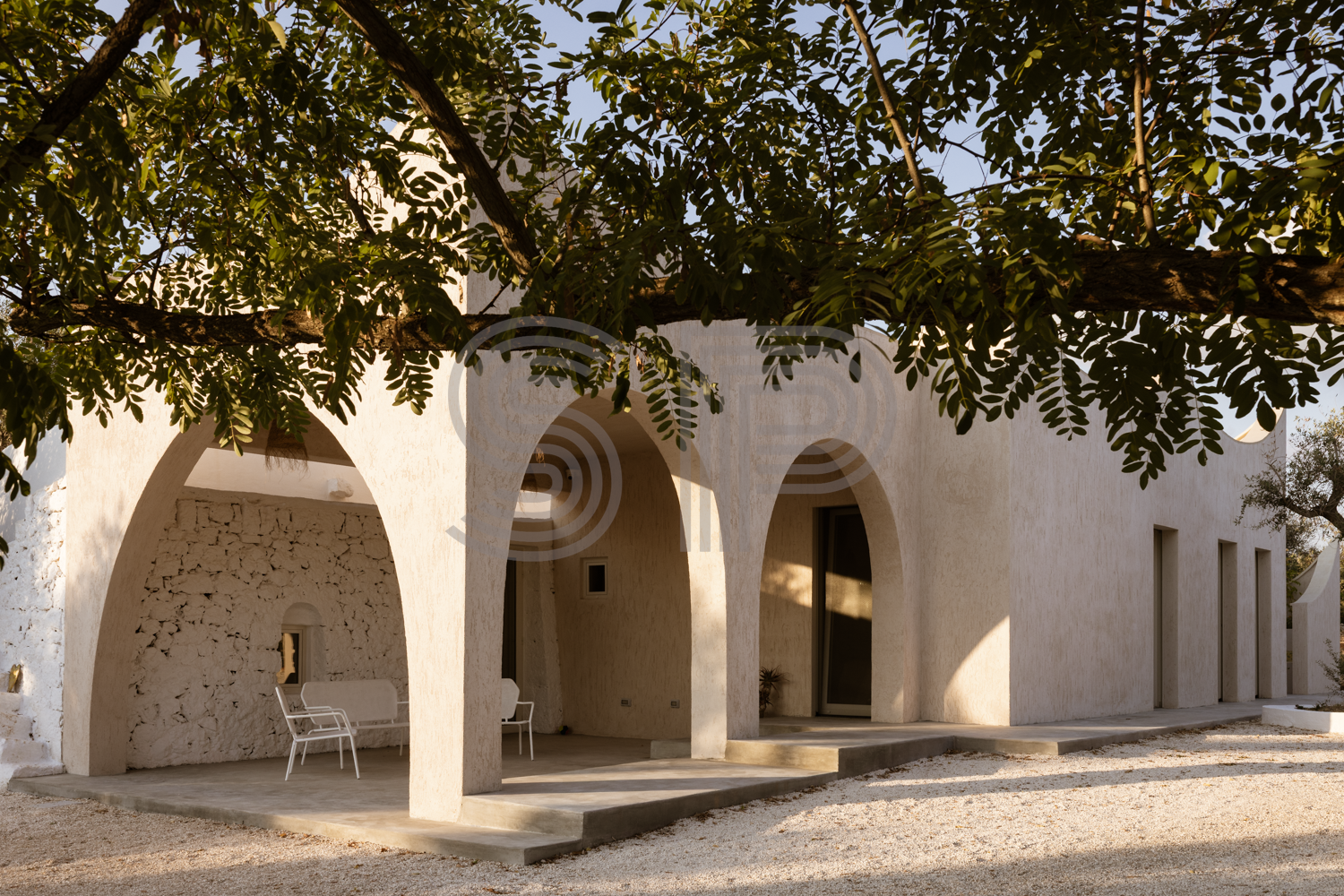 Contemporary Puglian villa with sculptural arched portico, textured lime walls and ancient trullo.