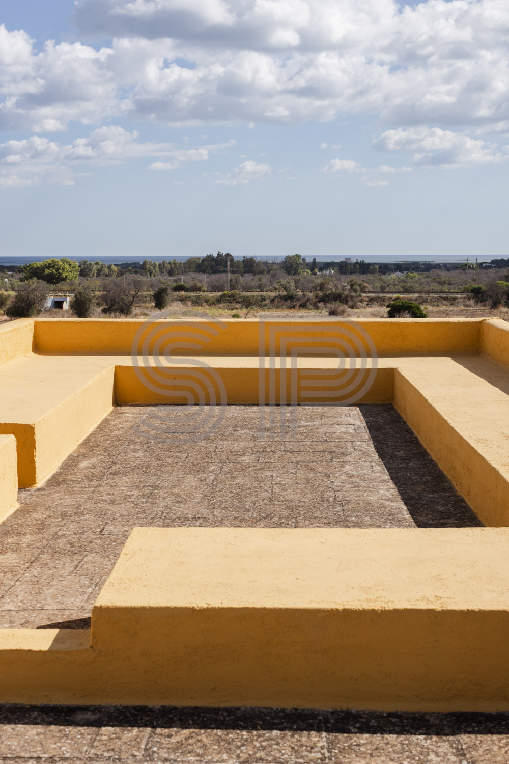 Contemporary Puglia villa roof terrace with bold yellow built-in seating, geometric architectural forms and distant sea views