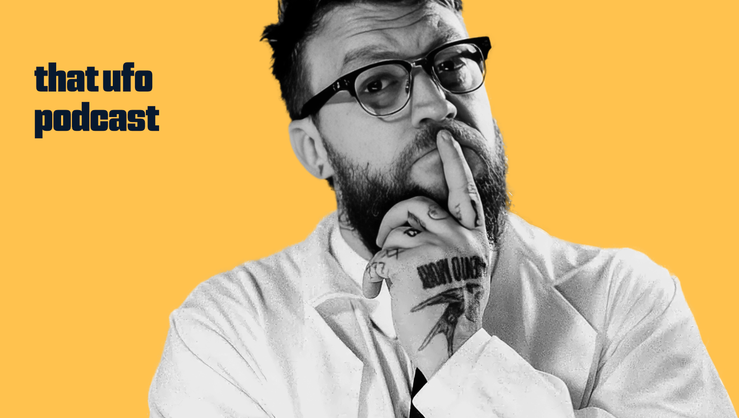A black-and-white photo of a man with glasses and a beard, with his hand on his face, tattoos visible on his fingers and hand, against a yellow background with text that reads 'that ufo podcast'.