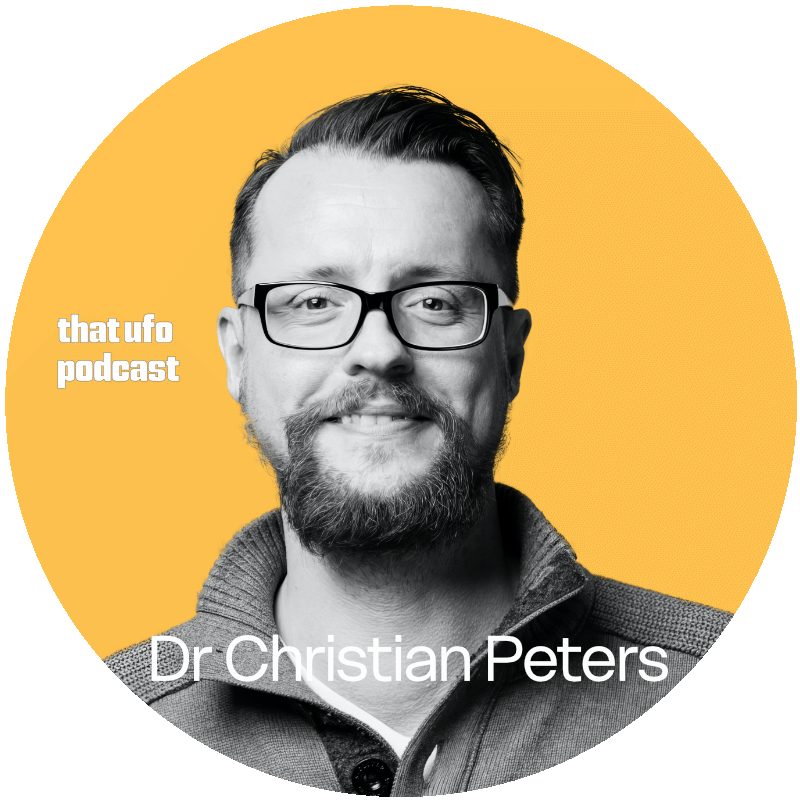 A man with glasses, a beard, and a mustache smiling at the camera, wearing a dark jacket with a zipper, against a yellow circular background. Text overlays identify him as Dr. Christian Peters and mention the 'that ufo podcast'.