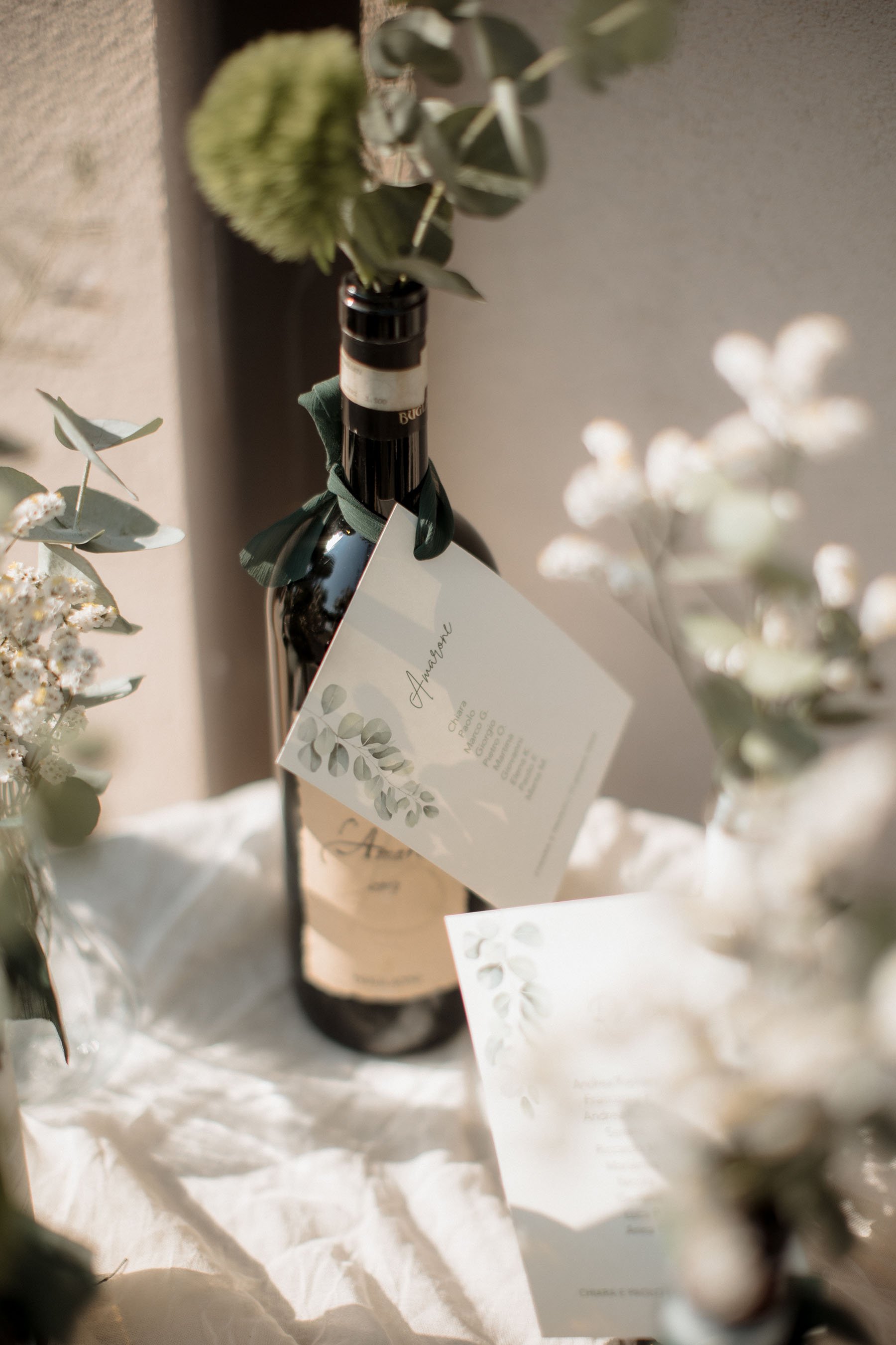 Bottiglia di vino decorata con un fiocco di nastro e fogli di carta con motivi di foglie.