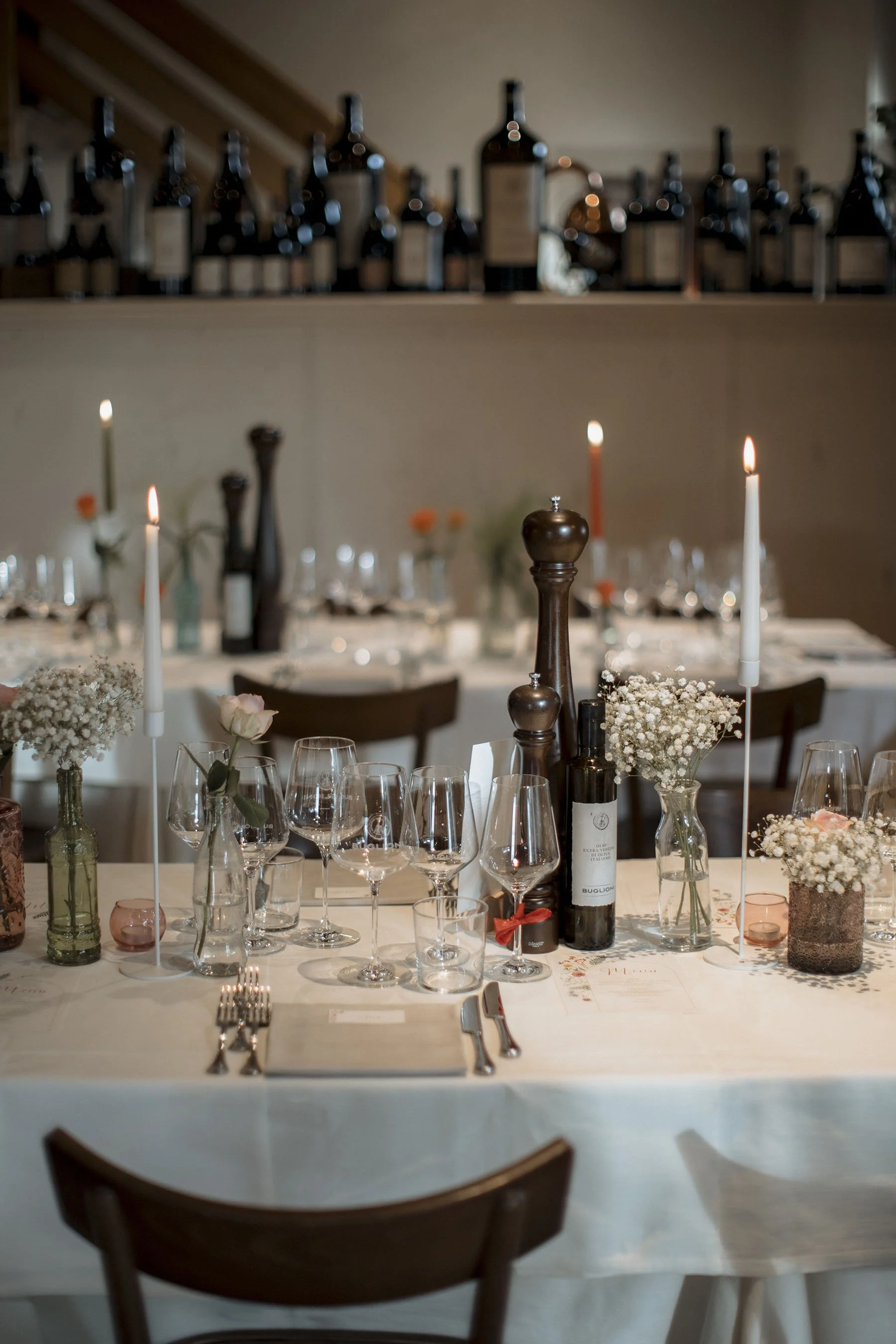 Tavola imbandita con bicchieri, piatti, posate, candele accese, fiori e bottiglie di vino, pronta per una cena elegante