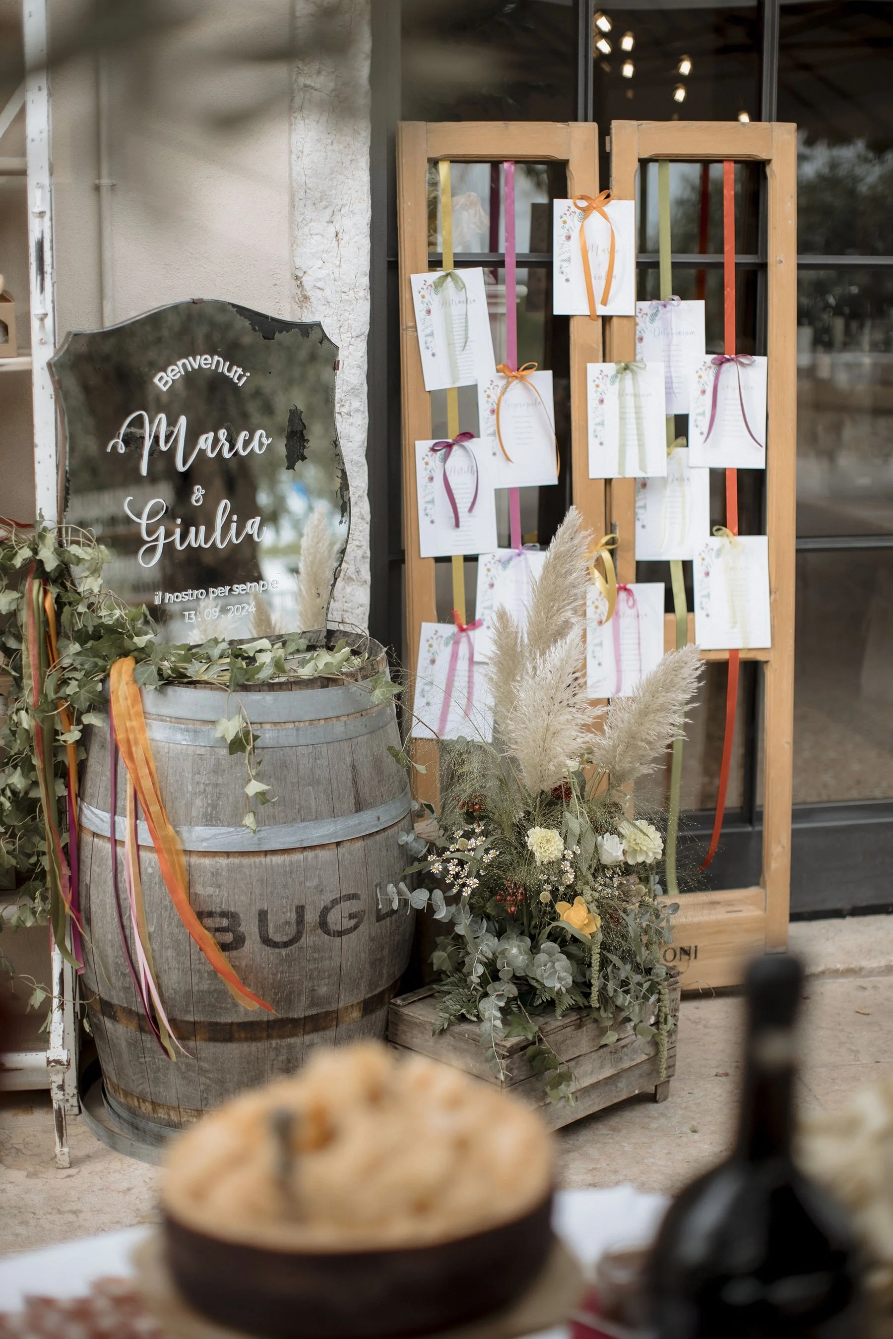 Carrozza di legno decorata con fiori e piante, tabella con scritta di benvenuto per Marco e Giulia, e una lavagna con la data del matrimonio, decorazioni con nastri colorati, in stile rustico.