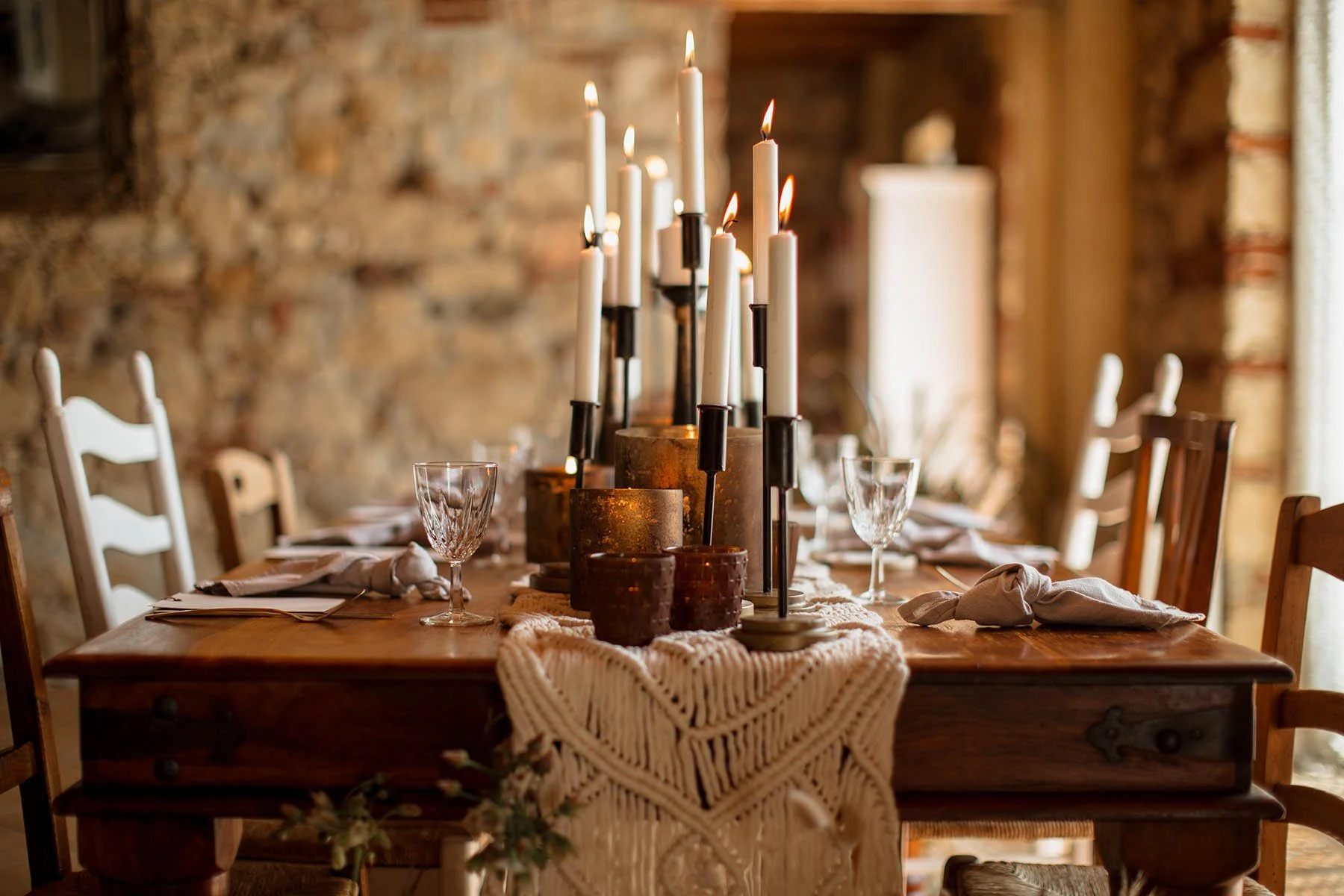 Tavolo da pranzo in stile rustico con centrotavola di candelabri con candele accese e bicchieri di cristallo, in un ambiente con pareti di pietra