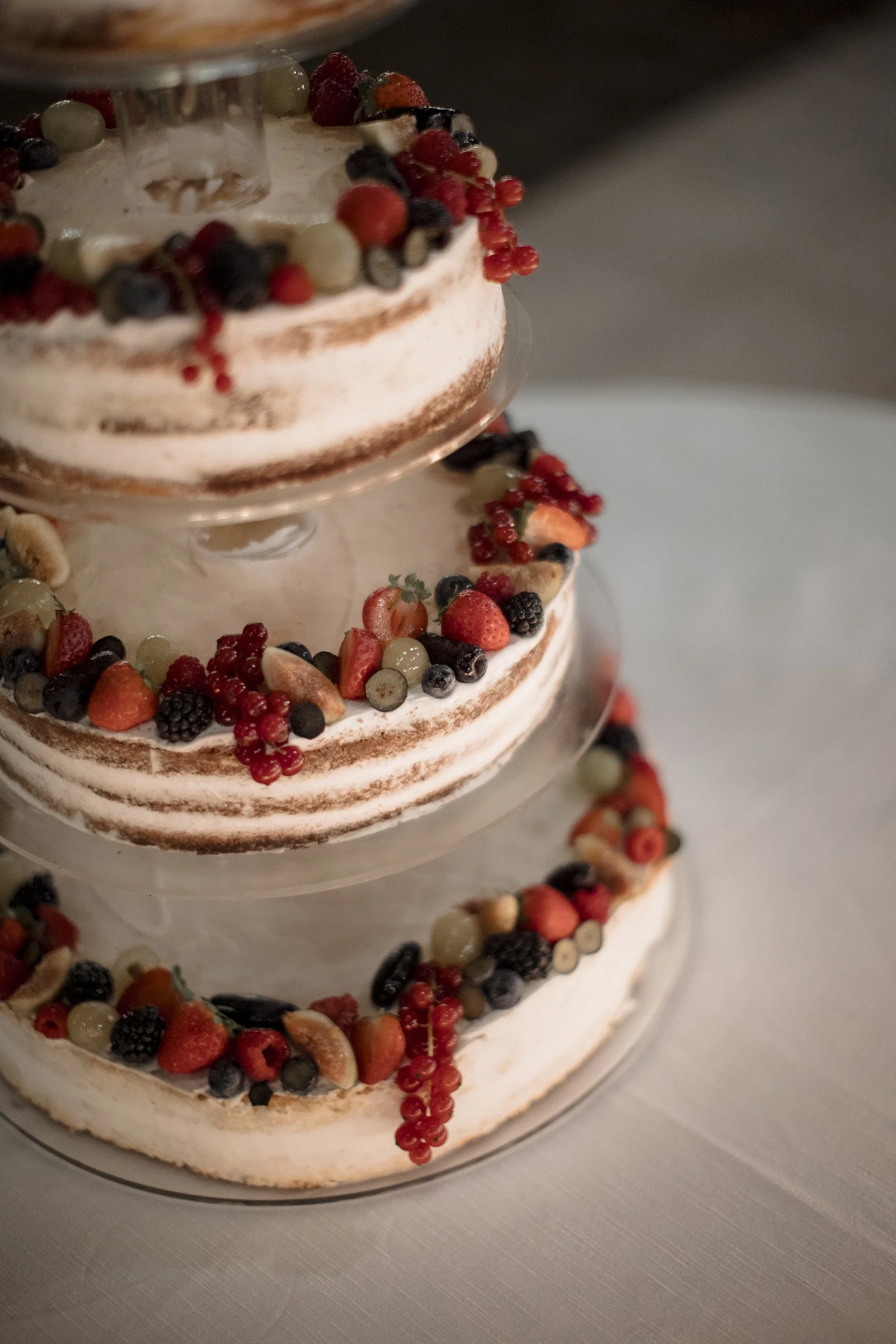 Torta nuziale a due piani decorata con frutti di bosco, come fragole, more, mirtilli e uva, e uno strato di panna, posizionata su un vassoio.