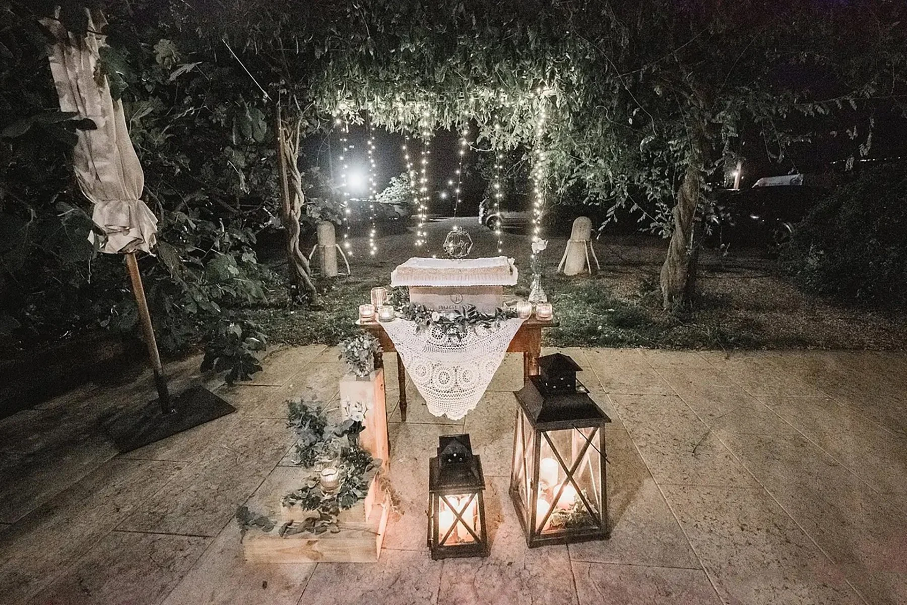 Decorazione per evento all'aperto con lanterne, tavolo con tovaglia ricamata, luci decorative e piante