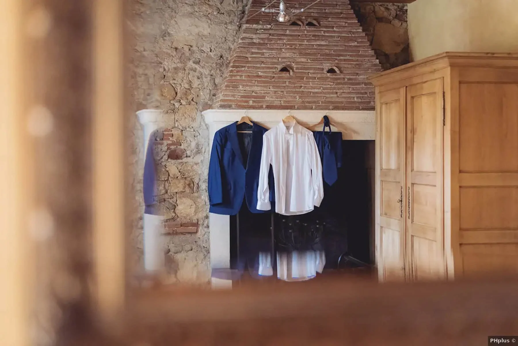 Armadio di legno vicino a una parete di mattoni e vestiti appesi su uno stendibiancheria, tra cui una giacca blu, una camicia bianca, e un cappotto blu scuro.