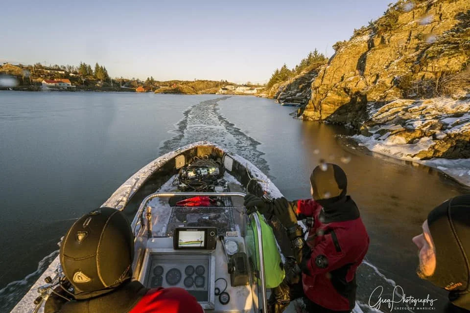 to dykkere som kjører en båt gjennom et tynt lag med is.