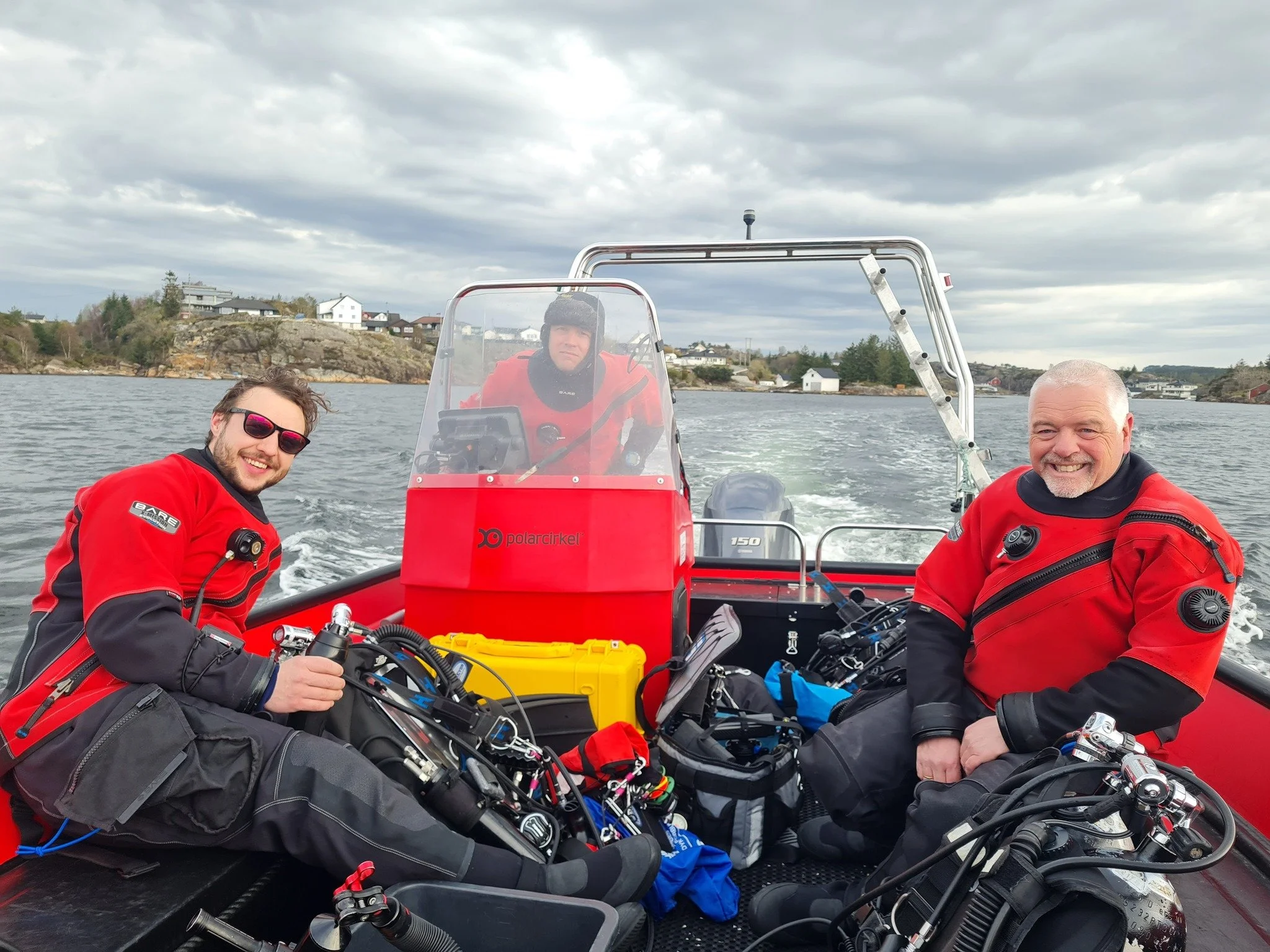 to dykkere i rød drakt kjører en rød polarcirkel båt.