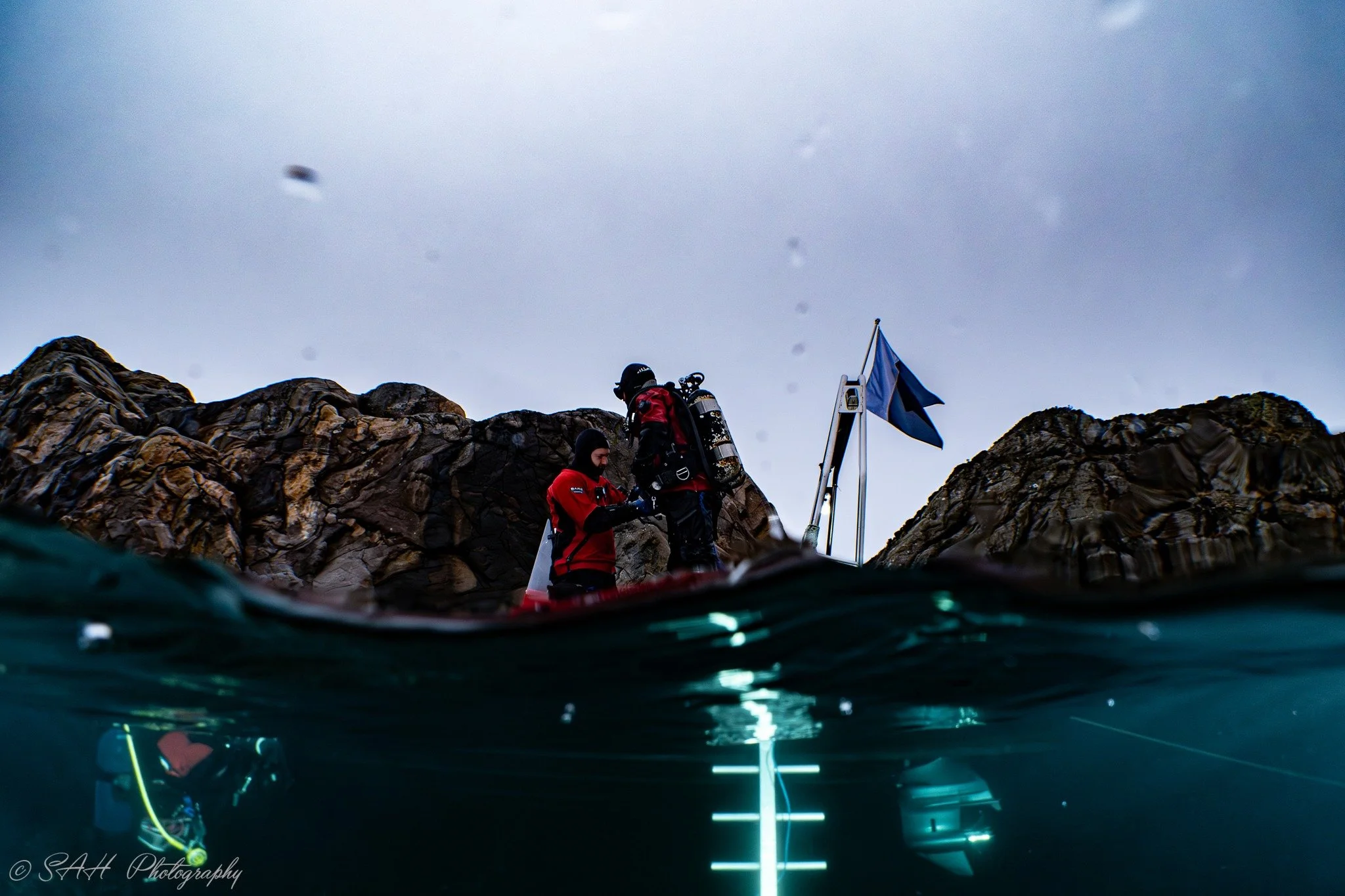 vinkel fra havet, hvor vi kan se to dykkere i en båt over vann og en dykker under vann.