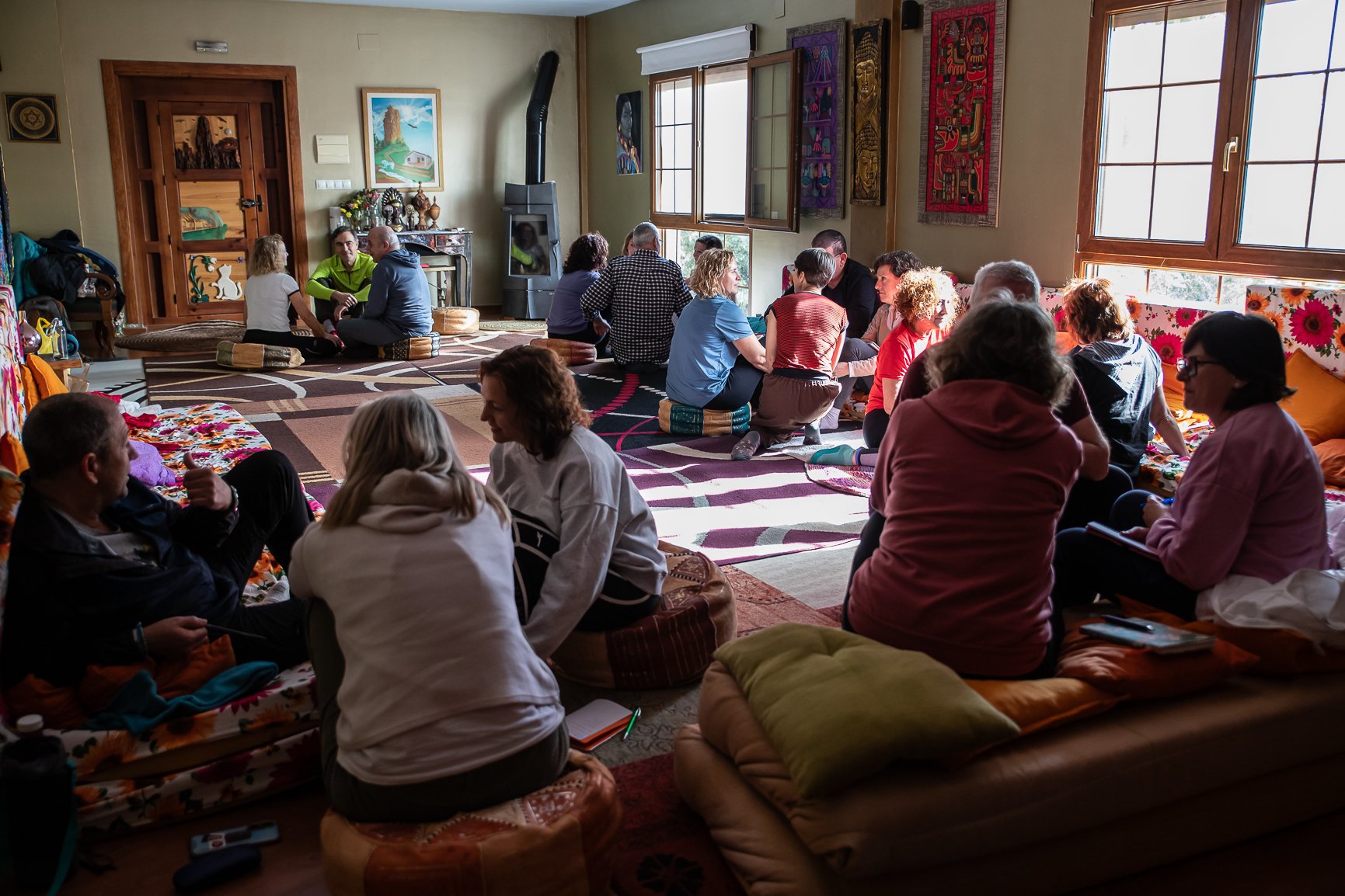 Grupo de personas sentadas en una alfombra en una sala decorada con arte y cortinas, participando en una actividad del retiro de desarrollo personal.