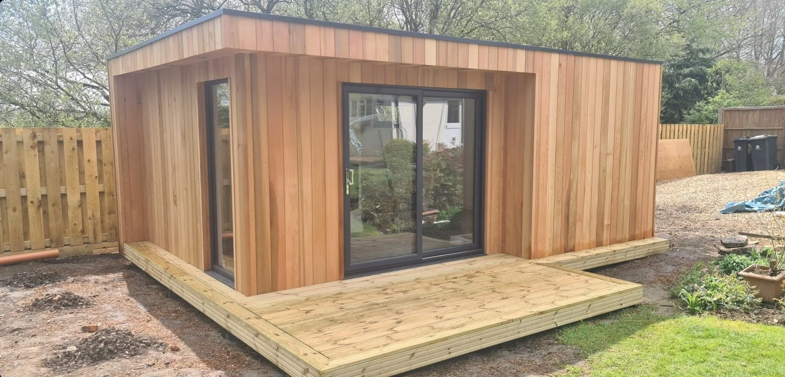 New wooden shed with sliding glass door on a small deck in a backyard.