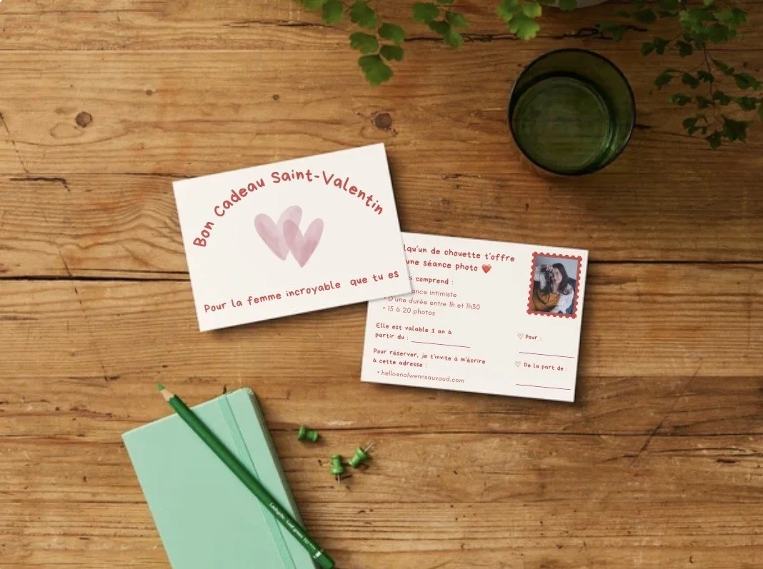 Carte de vœux de Saint-Valentin avec deux cœurs roses et message en français, un invité à un séance photo, un carnet vert avec un stylo vert, et un verre à moitié rempli, tous disposés sur une surface en bois