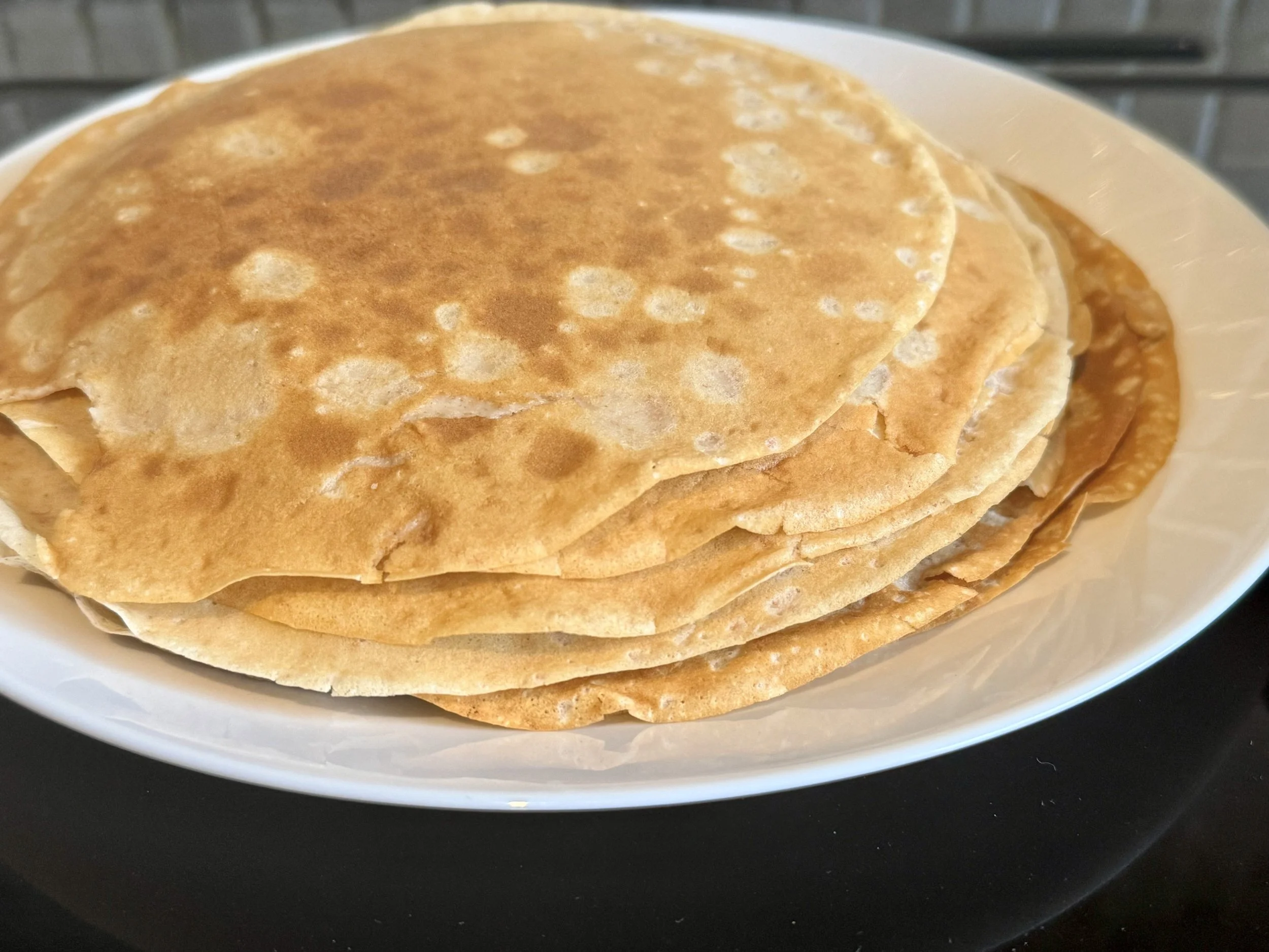 A stack of thin pancakes on a white plate.