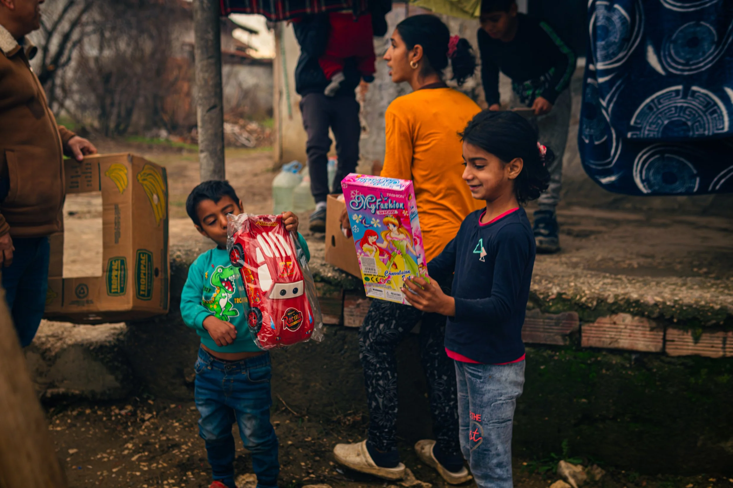 Två barn som står utomhus och öppnar julklappar som getts av Bulgarian Aid Mission, sponsrade av Agape Second Hand i Stockholm och Lidköping.