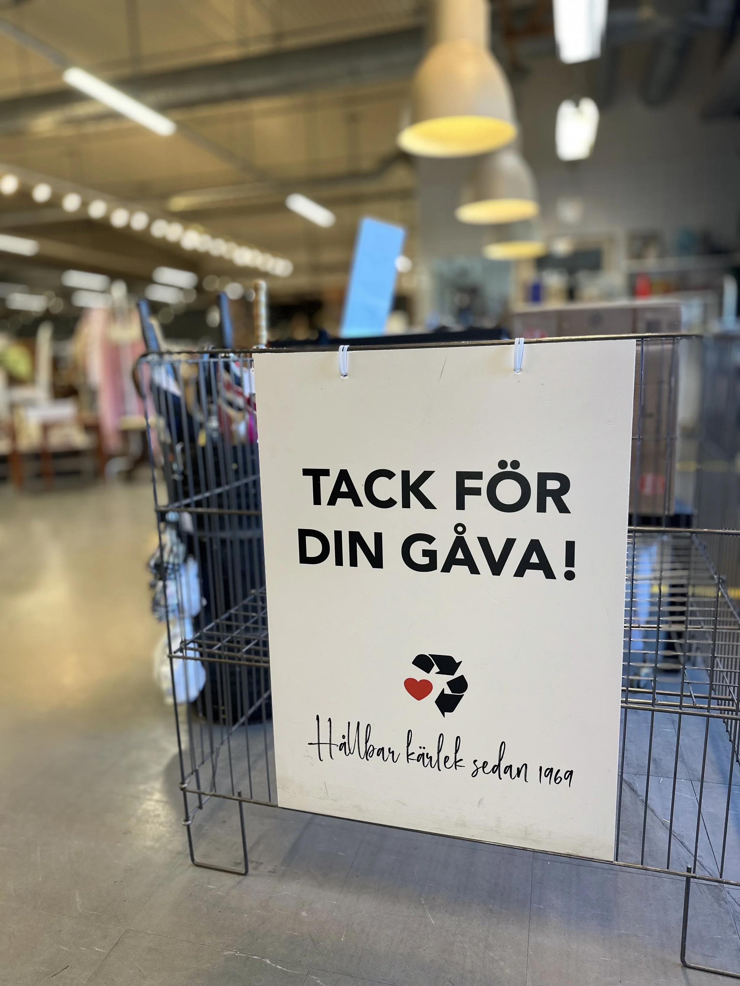 Sign in a store with Swedish text 'TACK FÖR DIN GÅVA! Hälsar kärlek sedan 1969' and a logo with a heart and recycling symbol.
