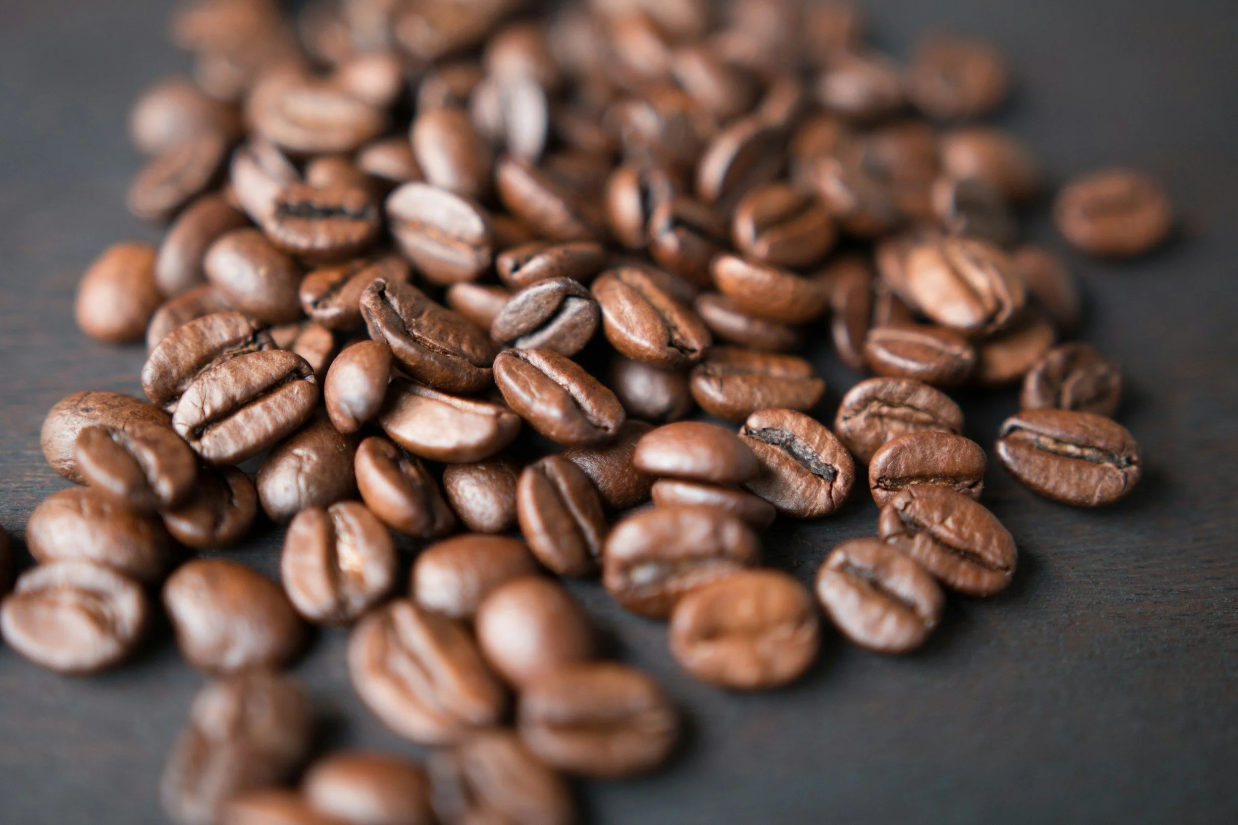 Close-up of roasted coffee beans scattered on a dark wooden surface.