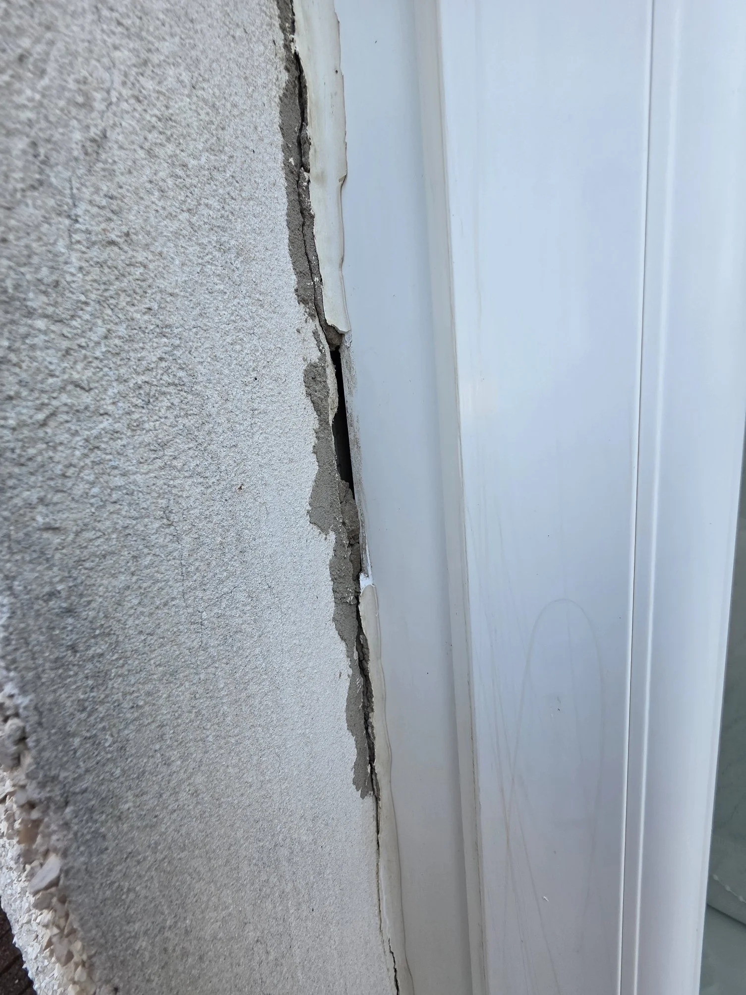 Close-up of a concrete foundation wall with visible cracks and a white siding wall attached to it.