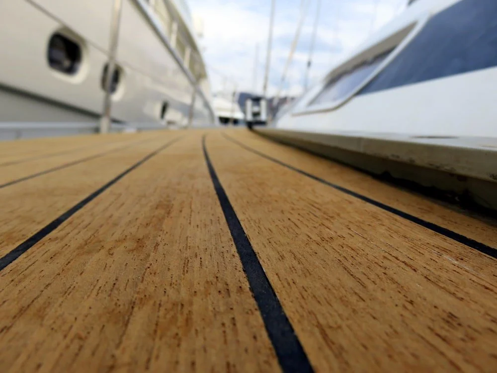 Close-up of a wooden boat deck with black lines, surrounded by boats with white hulls in a marina.