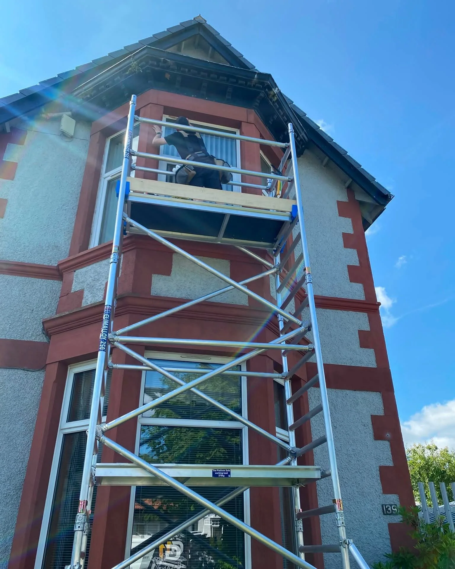 A person working on a building window while standing on a scaffold outside a house.