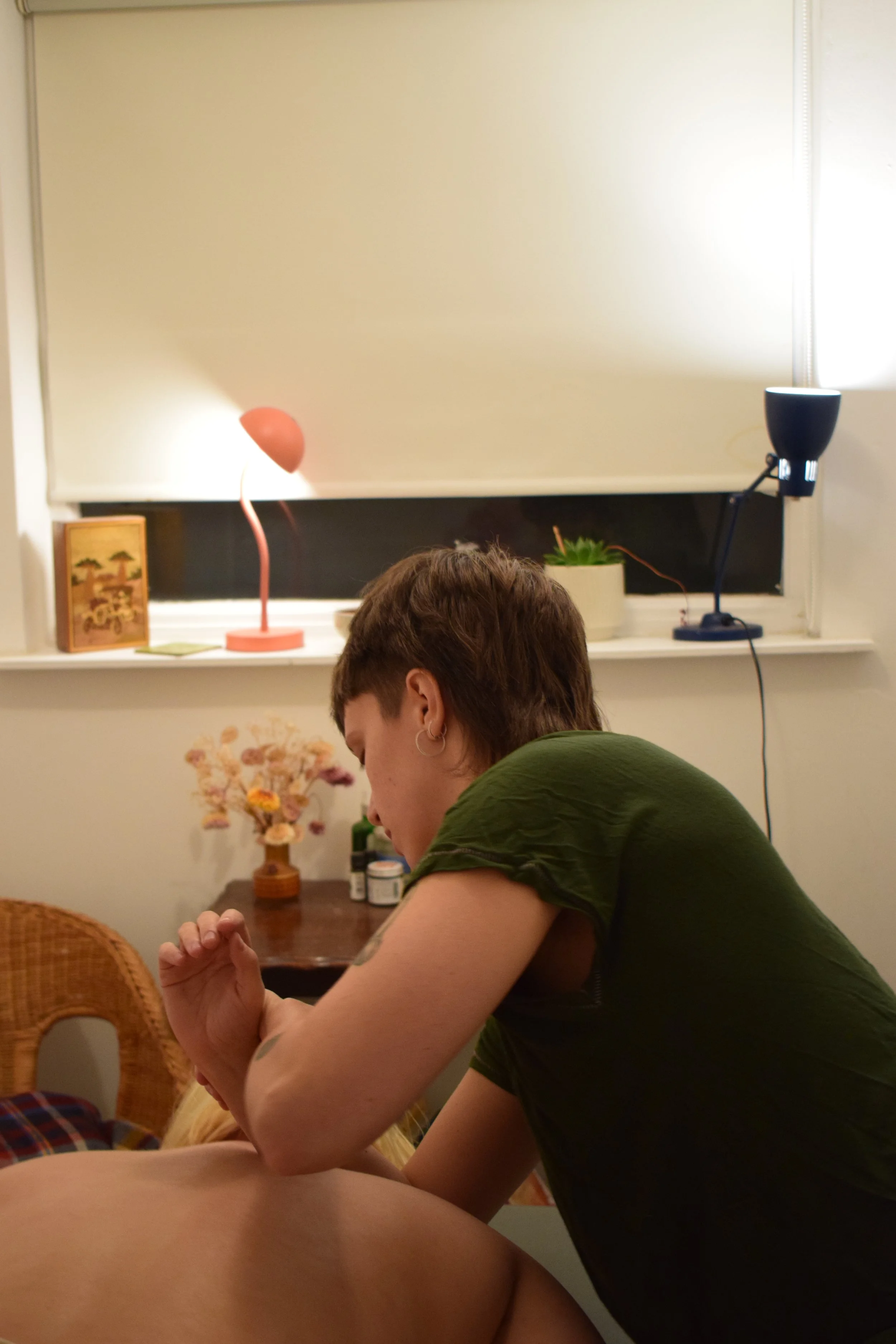 A person with short brown hair and earrings is giving a massage to someone in a cosy room