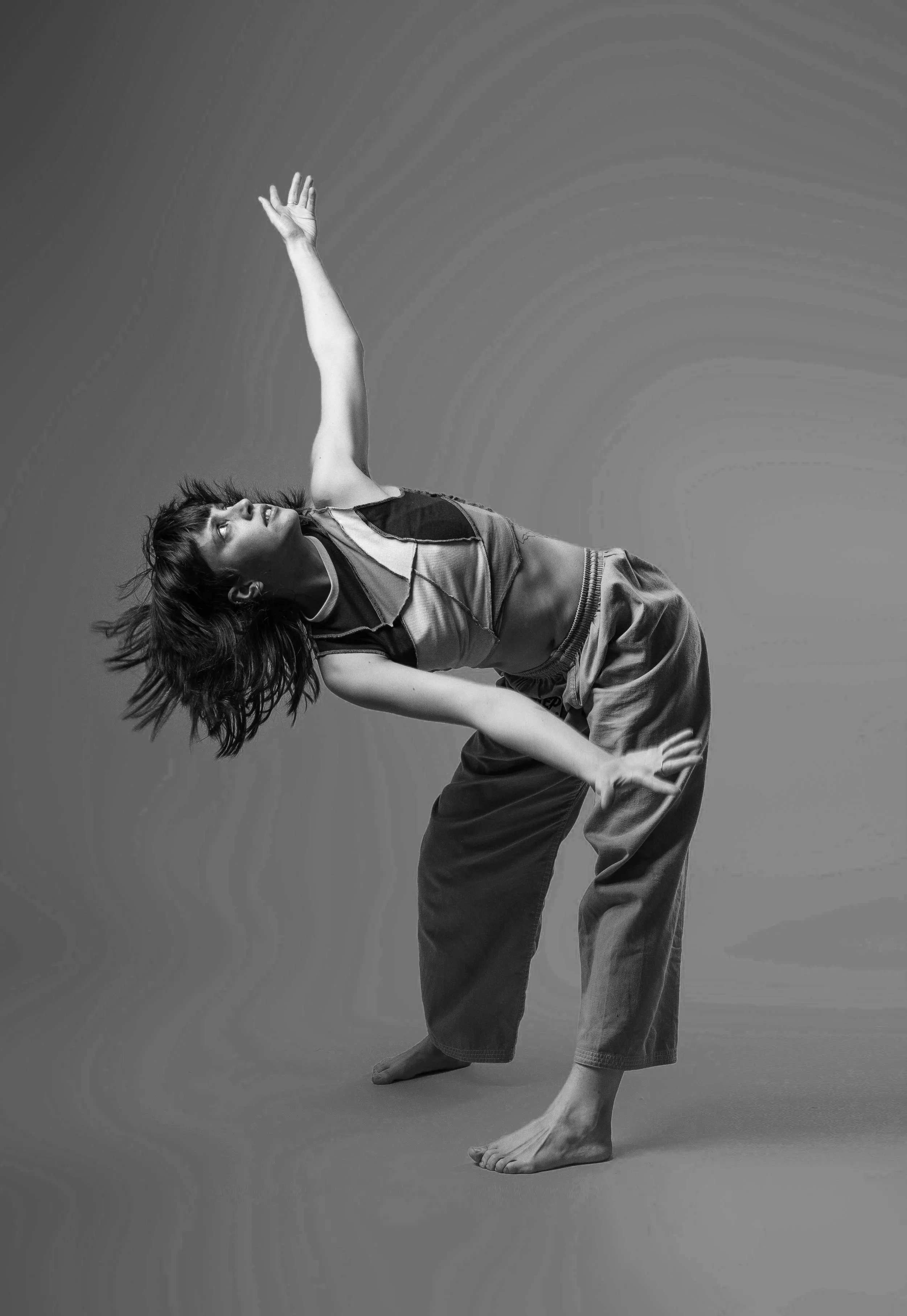 A woman dancing or performing a contemporary dance pose in a studio, wearing casual clothing, with her hair down, in black and white.