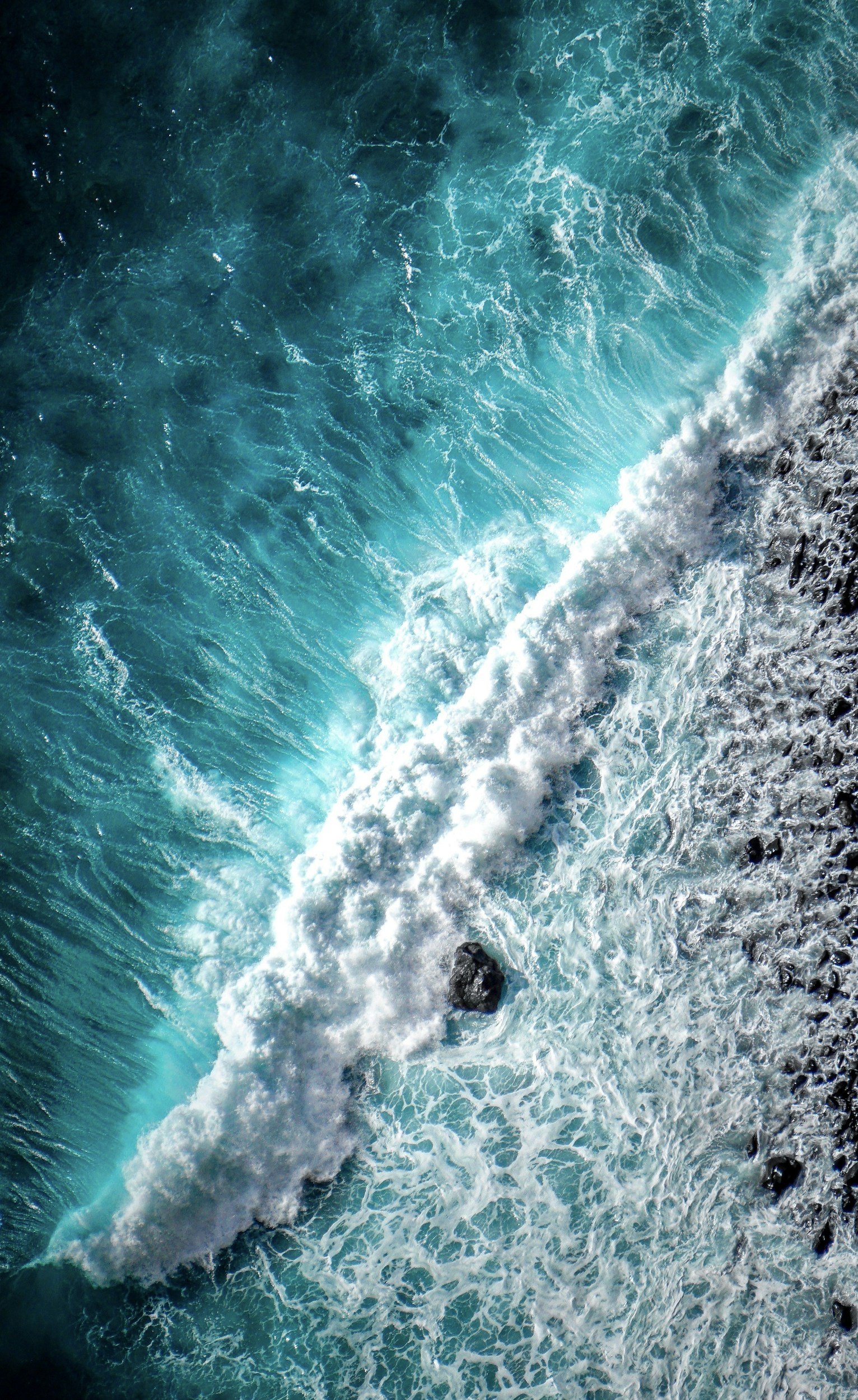 Aerial view of ocean waves crashing onto a rocky shoreline.