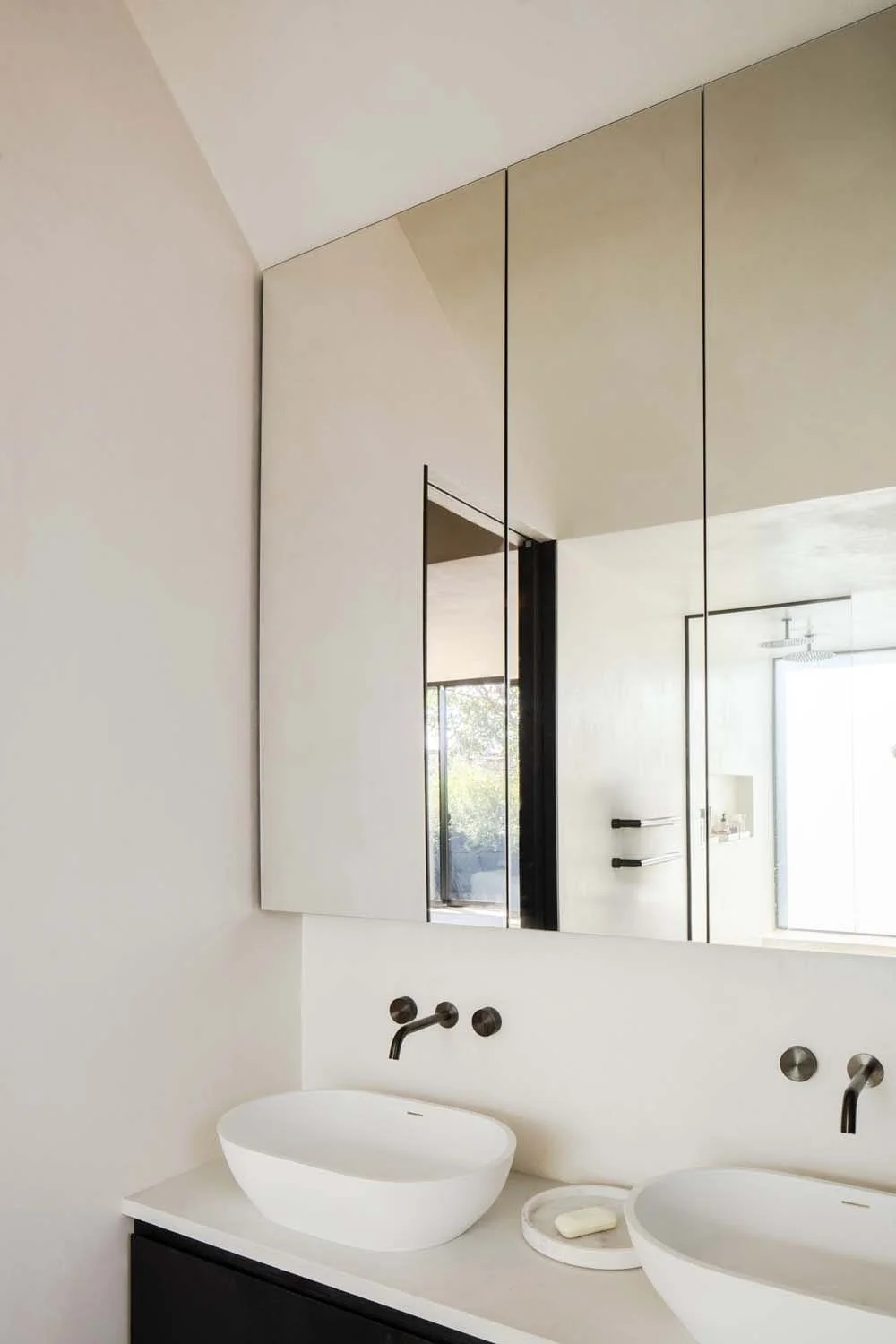 Contemporary double sinks with mirrored cabinet reflecting light. Elegant London architect interiors showcasing modern luxury