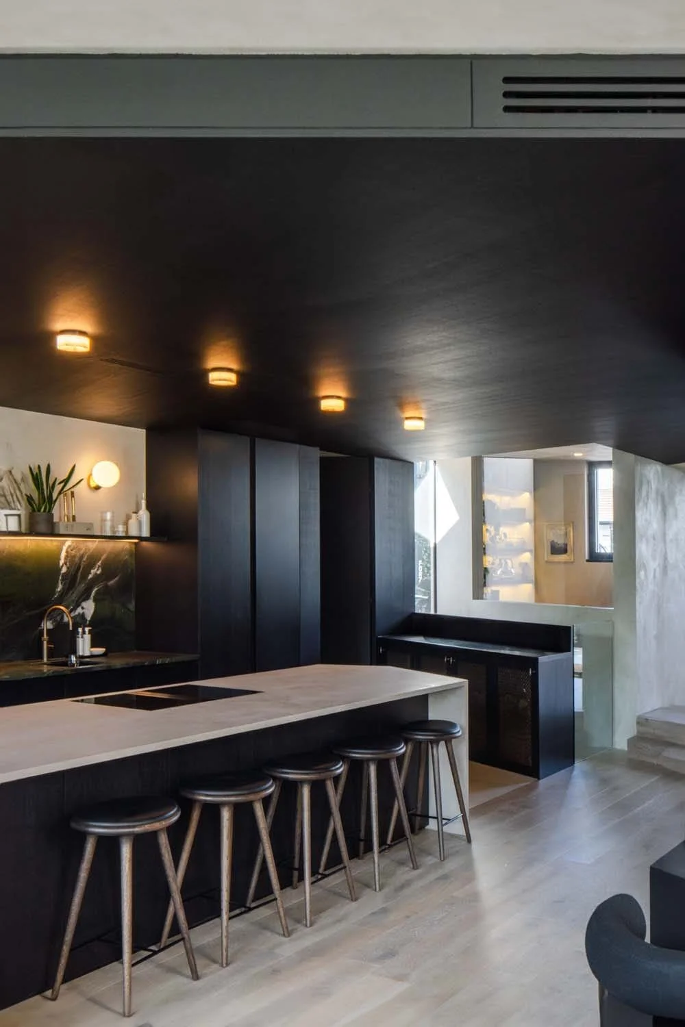 Black cabinets, green marble backsplash, and white island lit by integrated lights in a modern kitchen