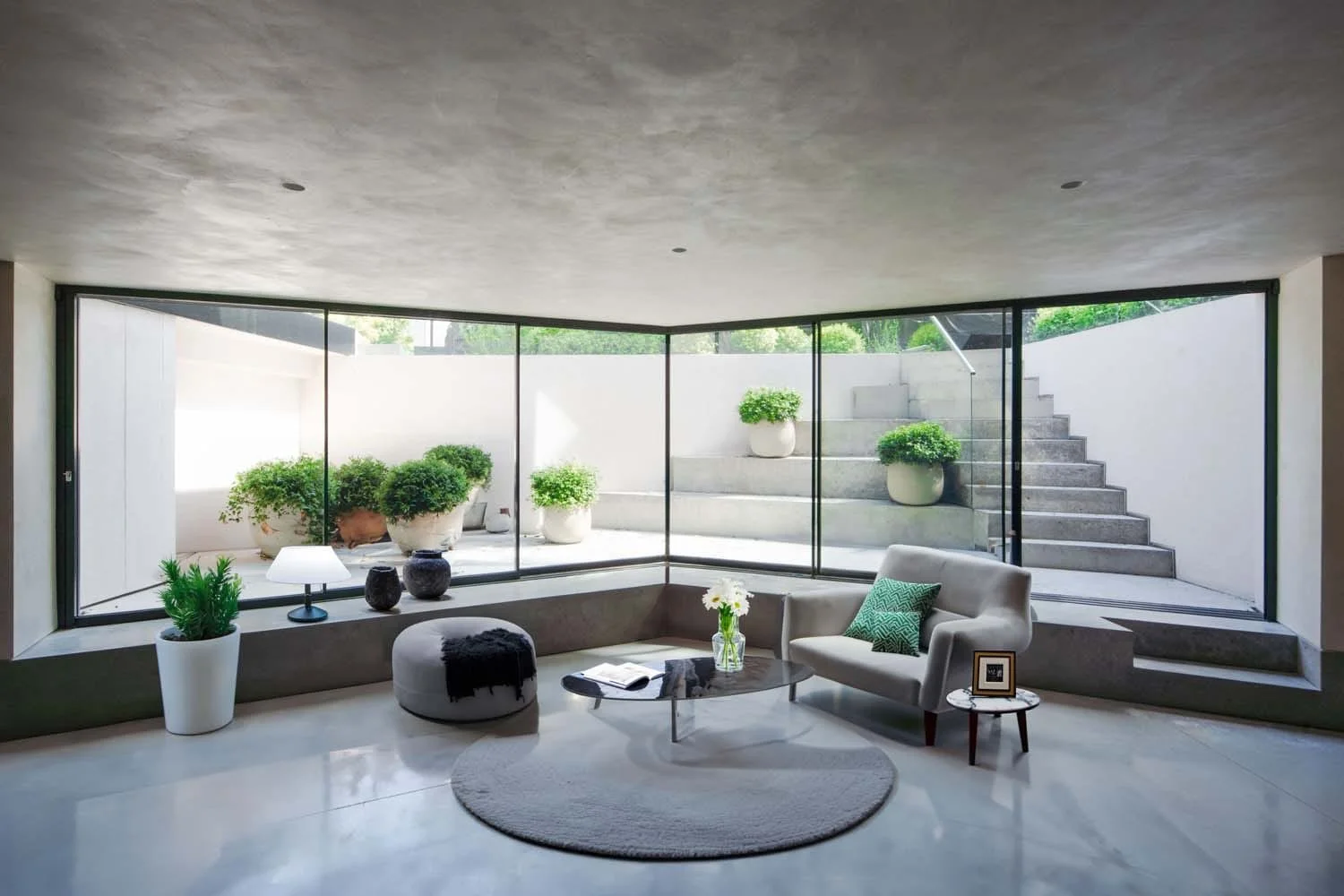 Wide view of modern lower ground lounge with garden backdrop. Contemporary residential elegance by a London luxury architect